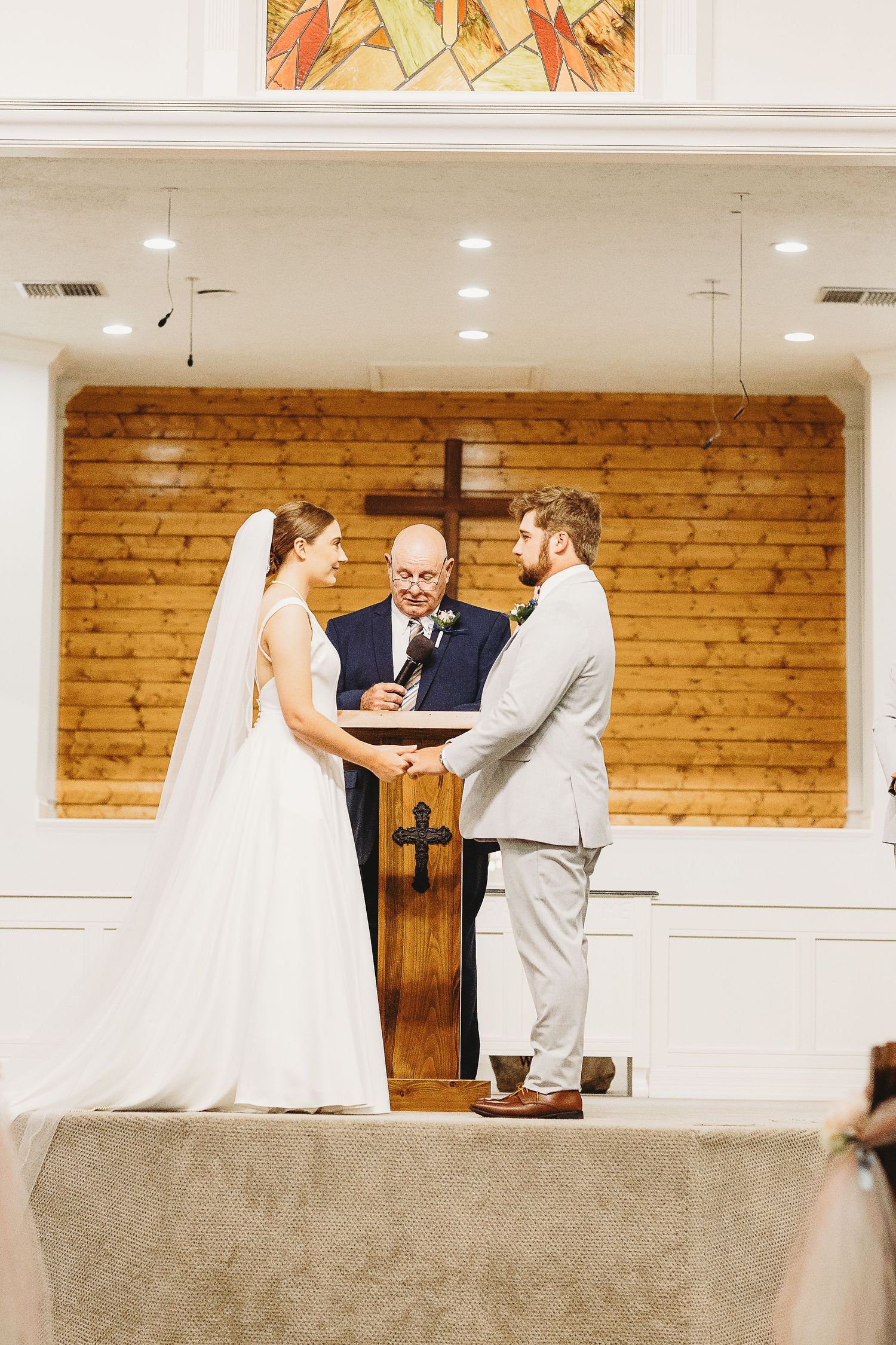 Wedding ceremony taking place in modern church sanctuary with wooden accent walls.