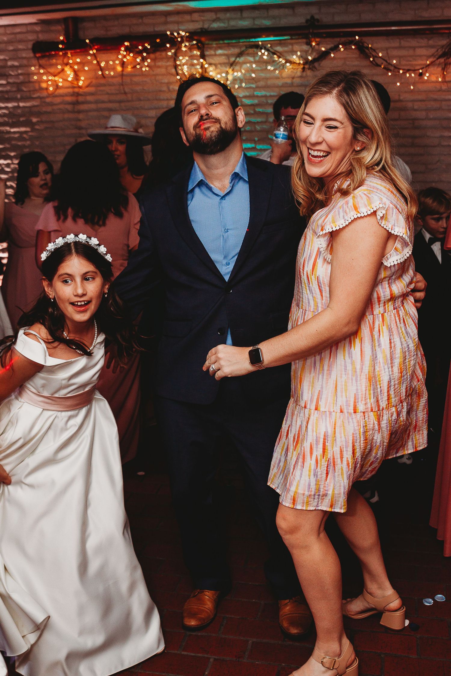 Guests enjoying themselves on the dance floor at a wedding reception with string lights overhead.