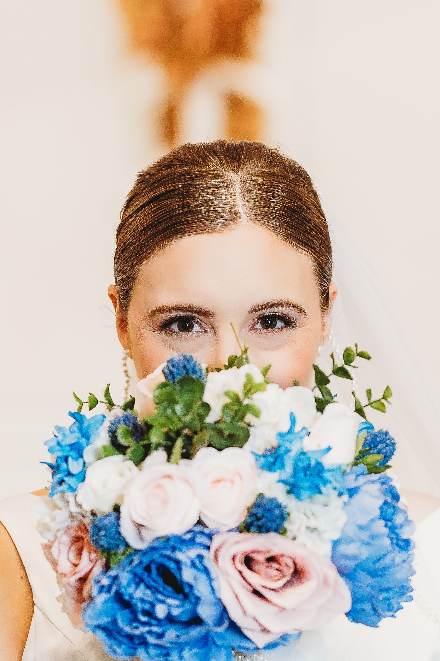 Close-up shot of eyes peeking over blue and pink floral bouquet.