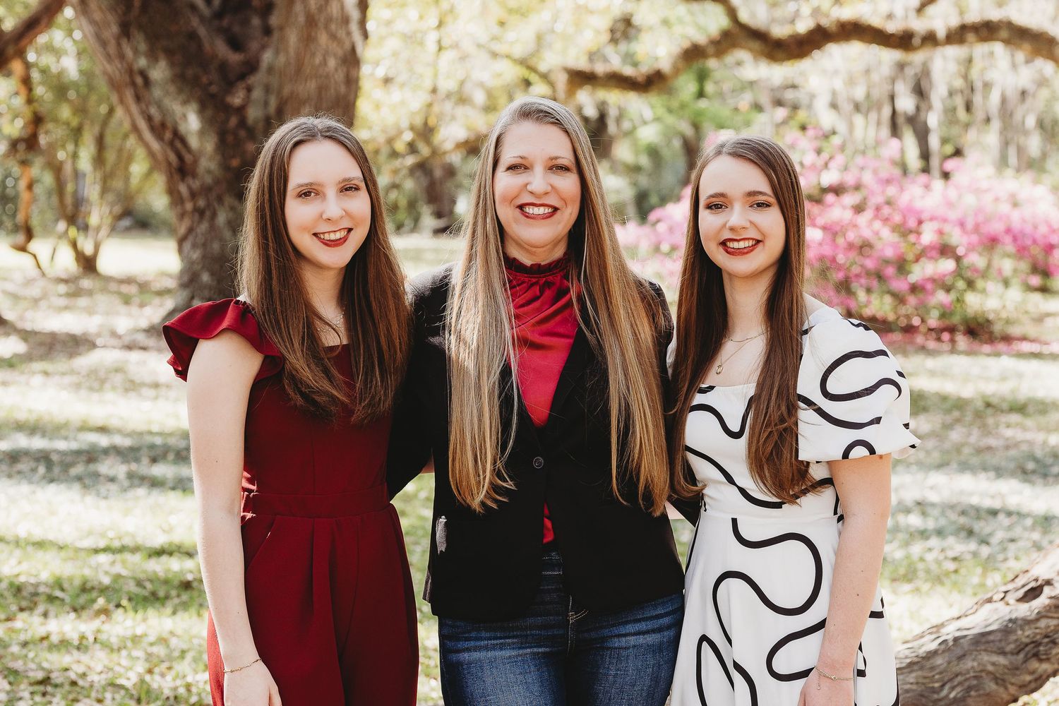 Family members in burgundy and white outfits pose together under oak trees during an outdoor photo session.