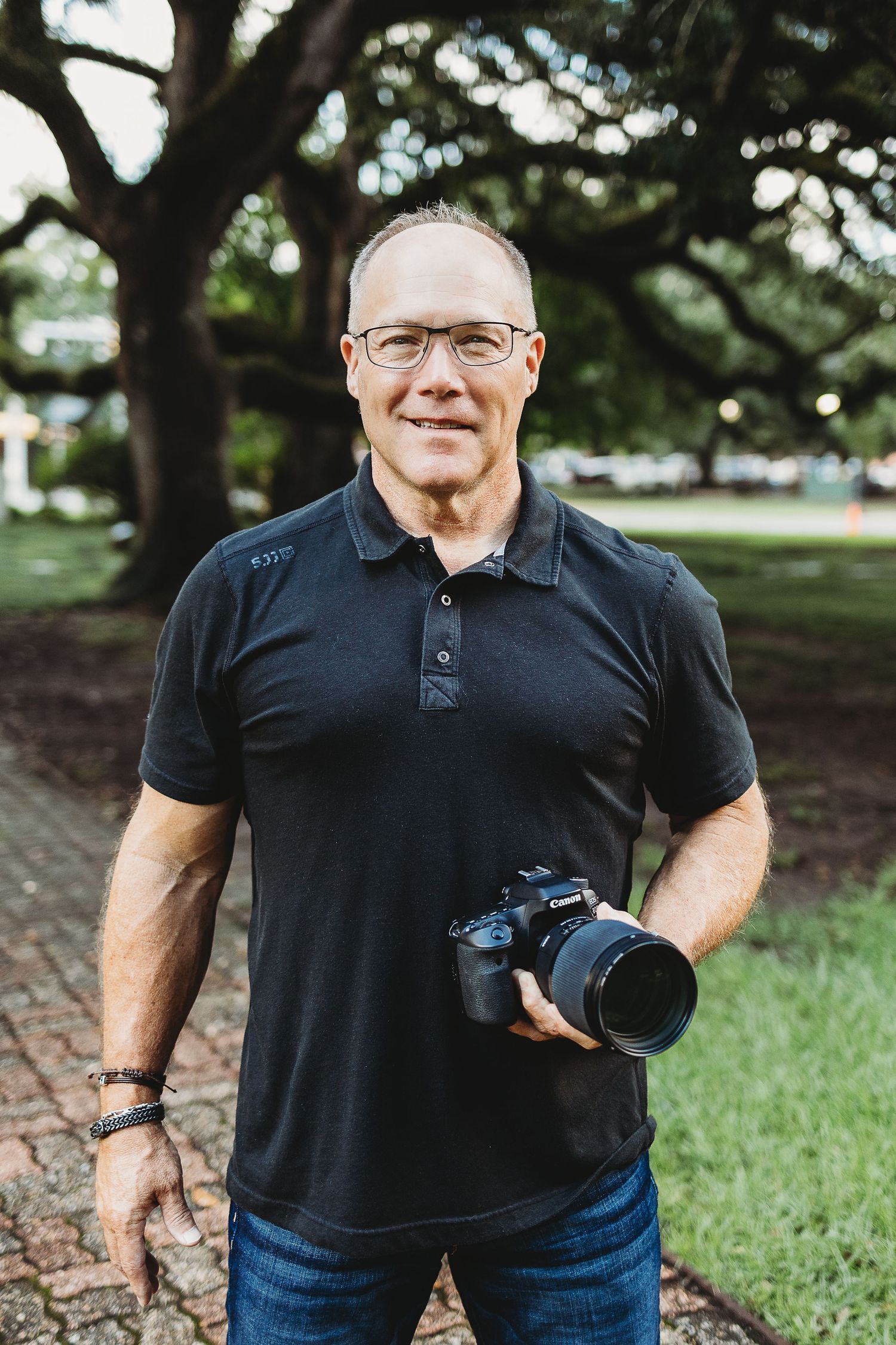 Professional photographer in black polo shirt holding camera equipment outdoors.