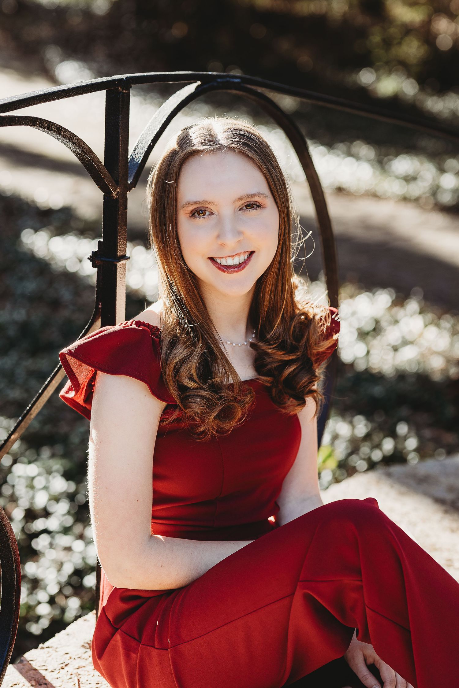 Portrait in red formal dress seated under decorative metal archway.