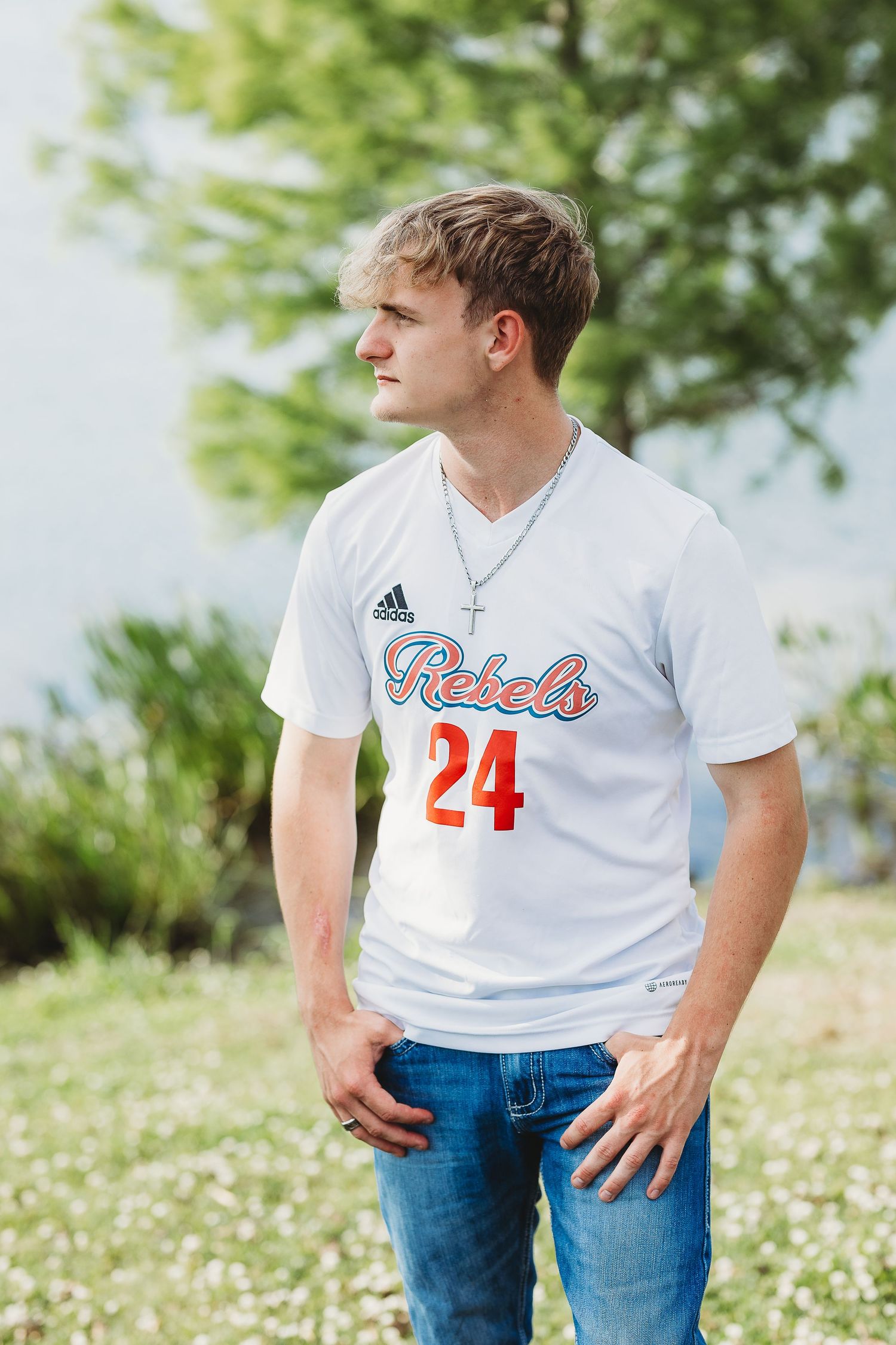 Senior portrait in white baseball jersey with number 24 against natural background.