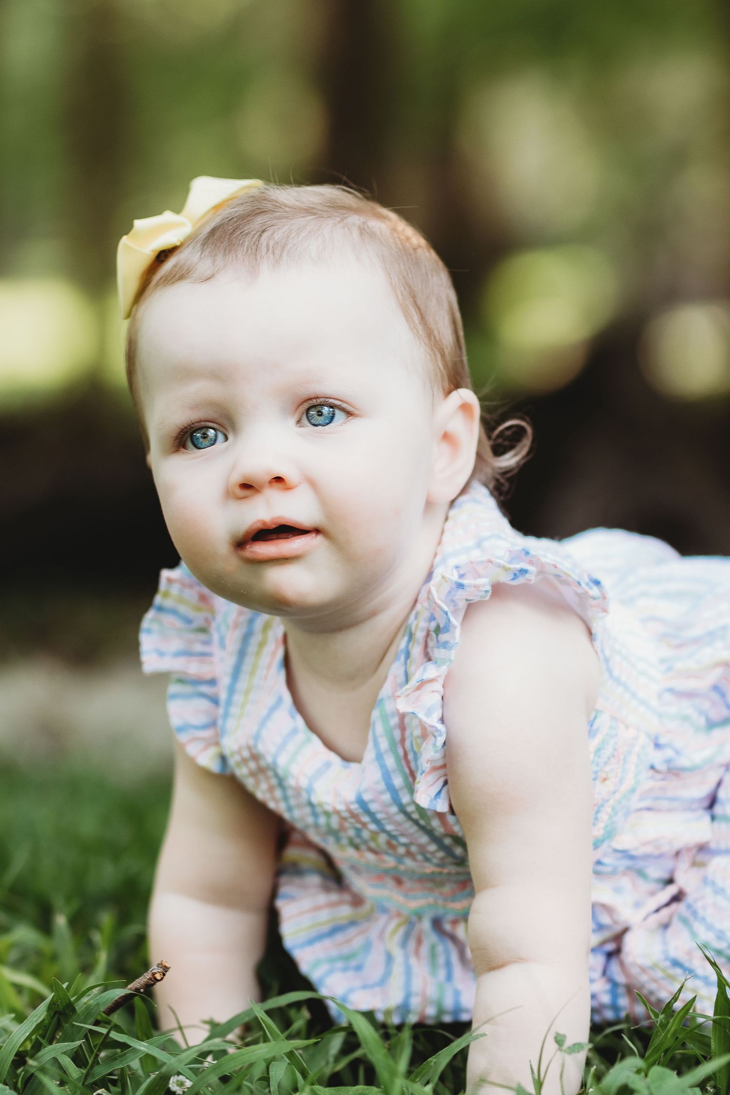 Baby in floral dress crawling on green grass during outdoor photoshoot.