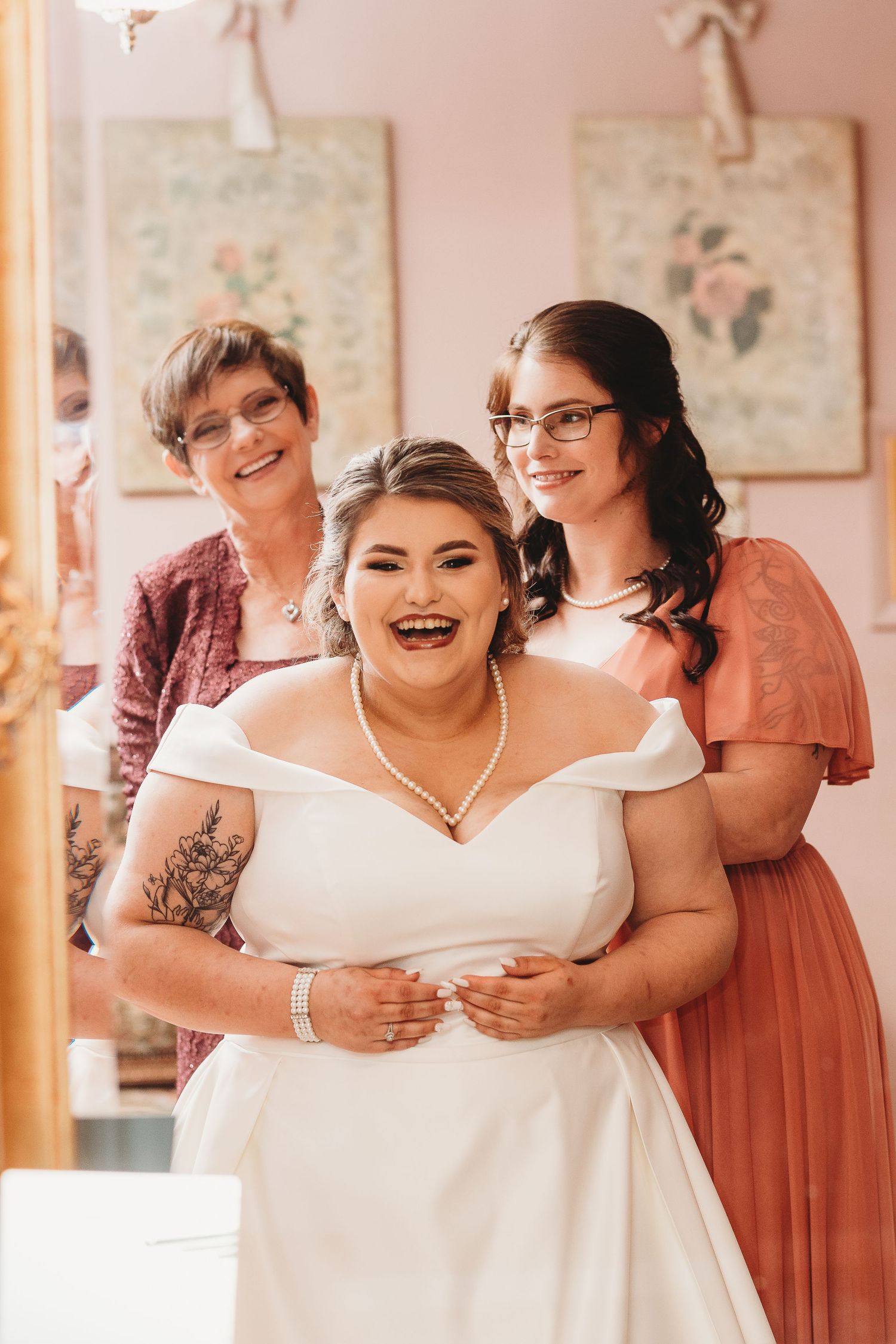 Wedding preparation scene with bridesmaids in coral dresses helping with final touches.