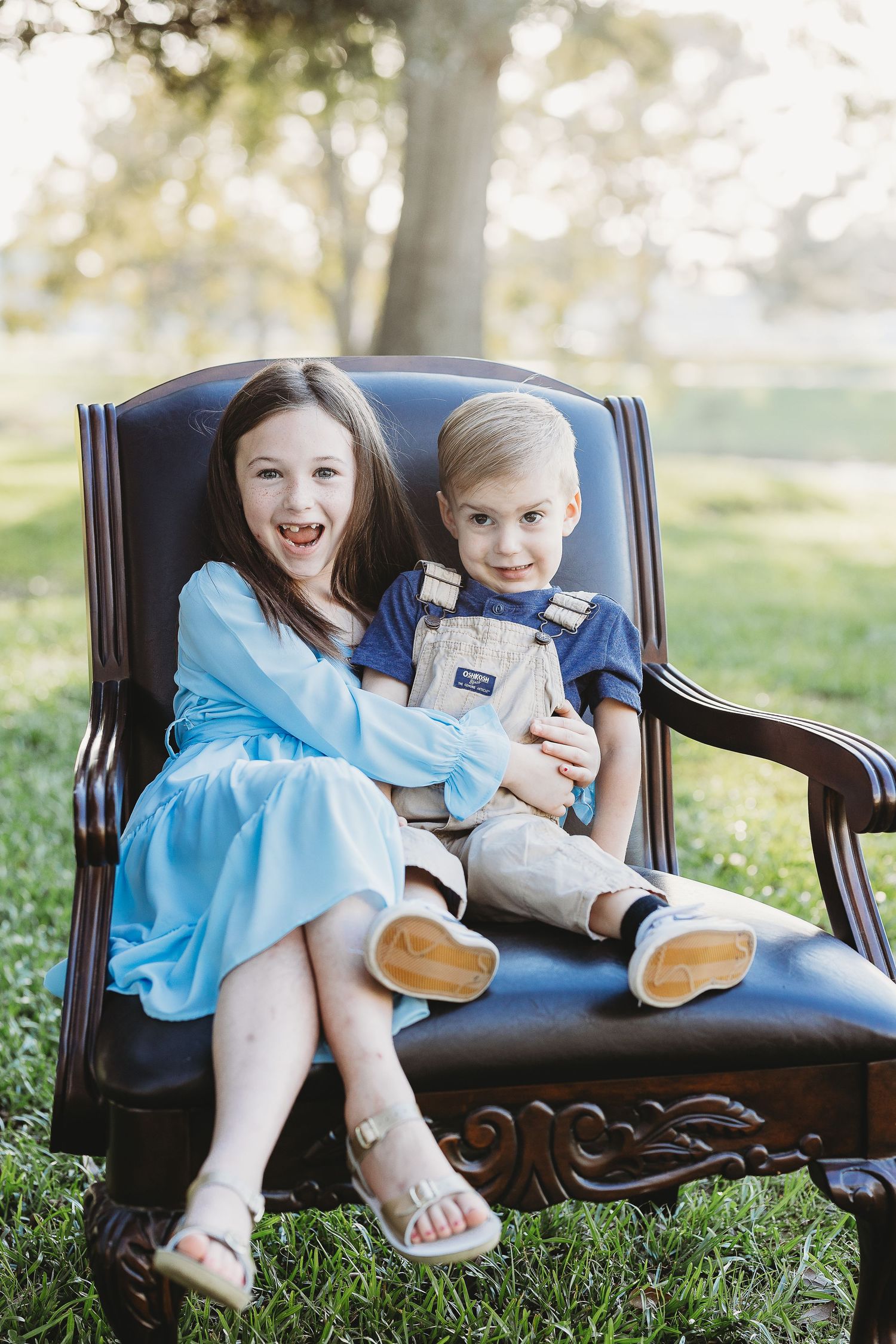 Children playing and laughing together on leather chair in garden setting.