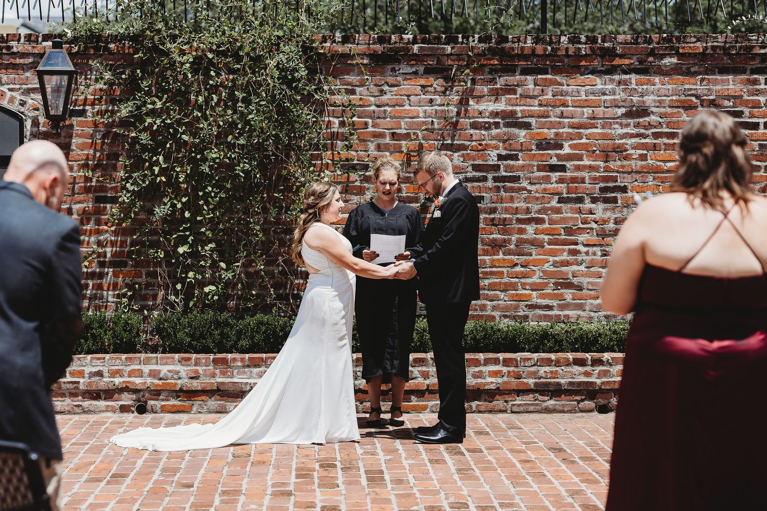 Outdoor wedding ceremony in front of historic brick wall with climbing vines.