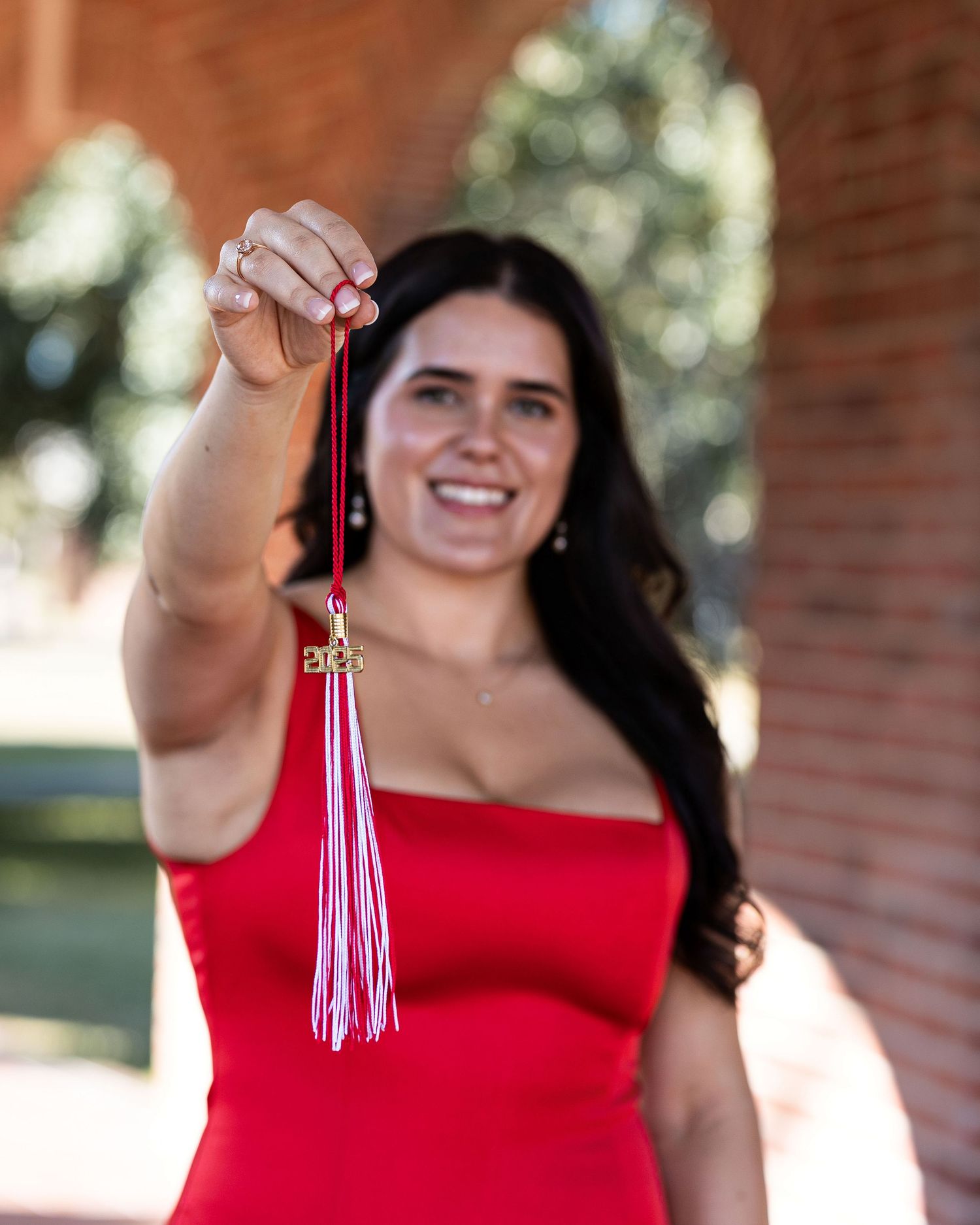 A graduate in a red dress holds up and displays their graduation tassel in a series of celebratory poses.