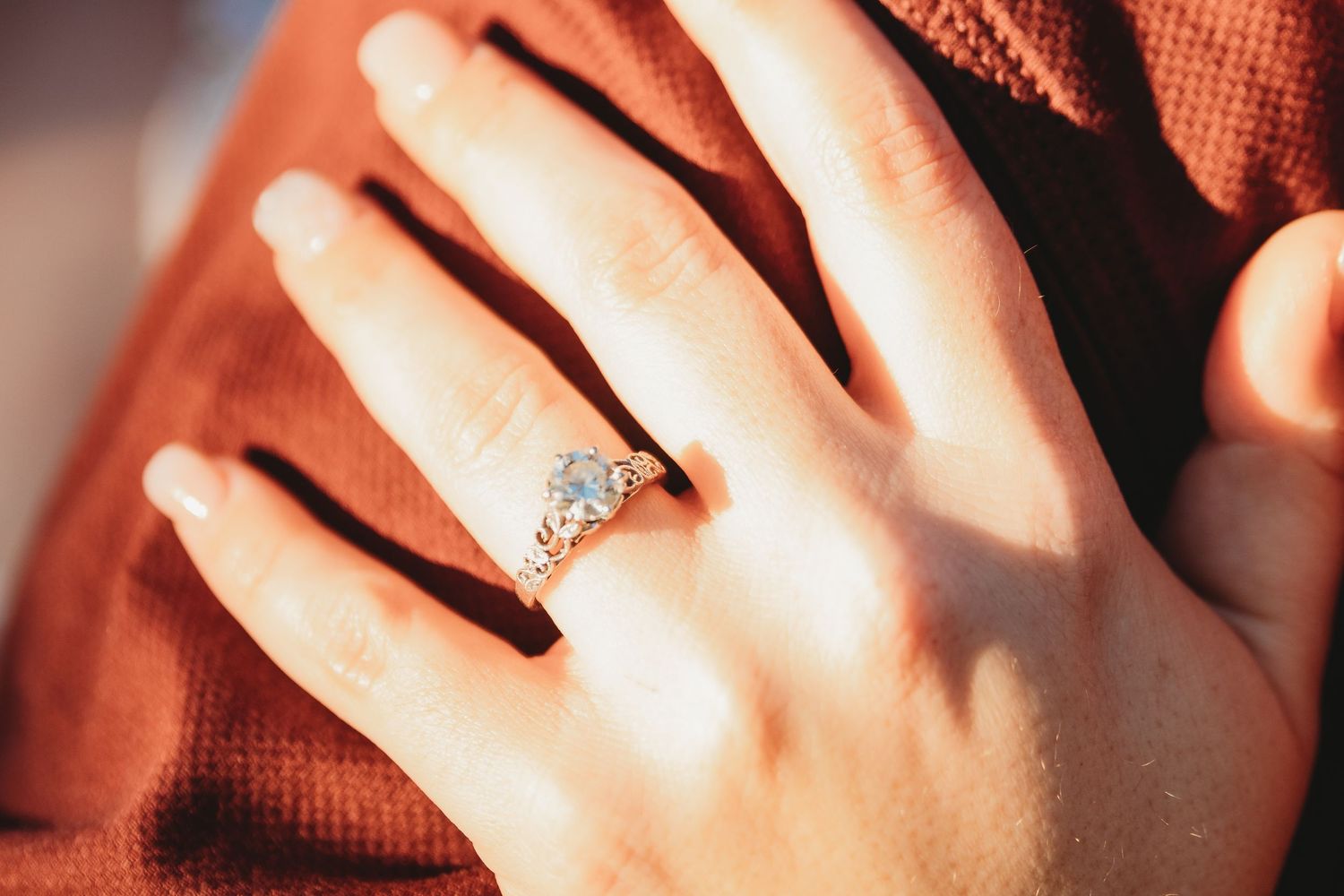 Close-up shot of hands with engagement ring in warm lighting.