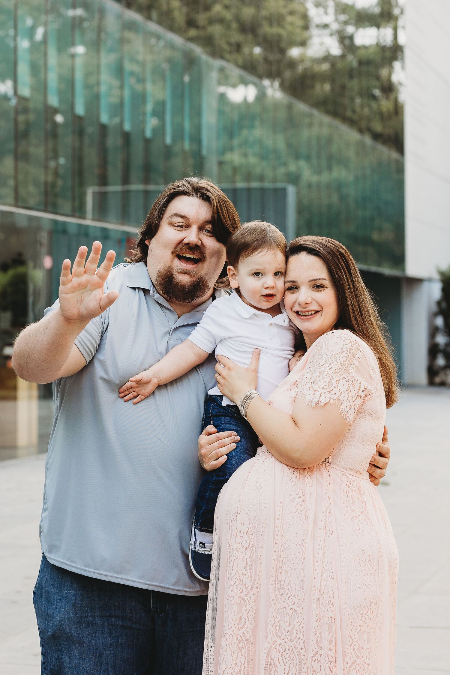 Playful family portrait with animated expressions against glass building backdrop.