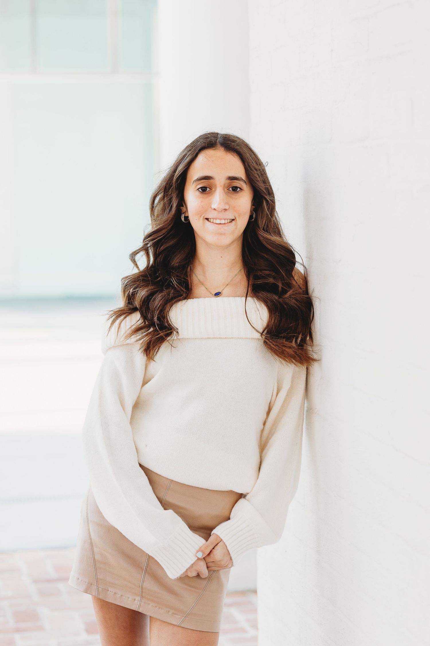 Person in cream colored outfit poses gracefully against white architectural background.