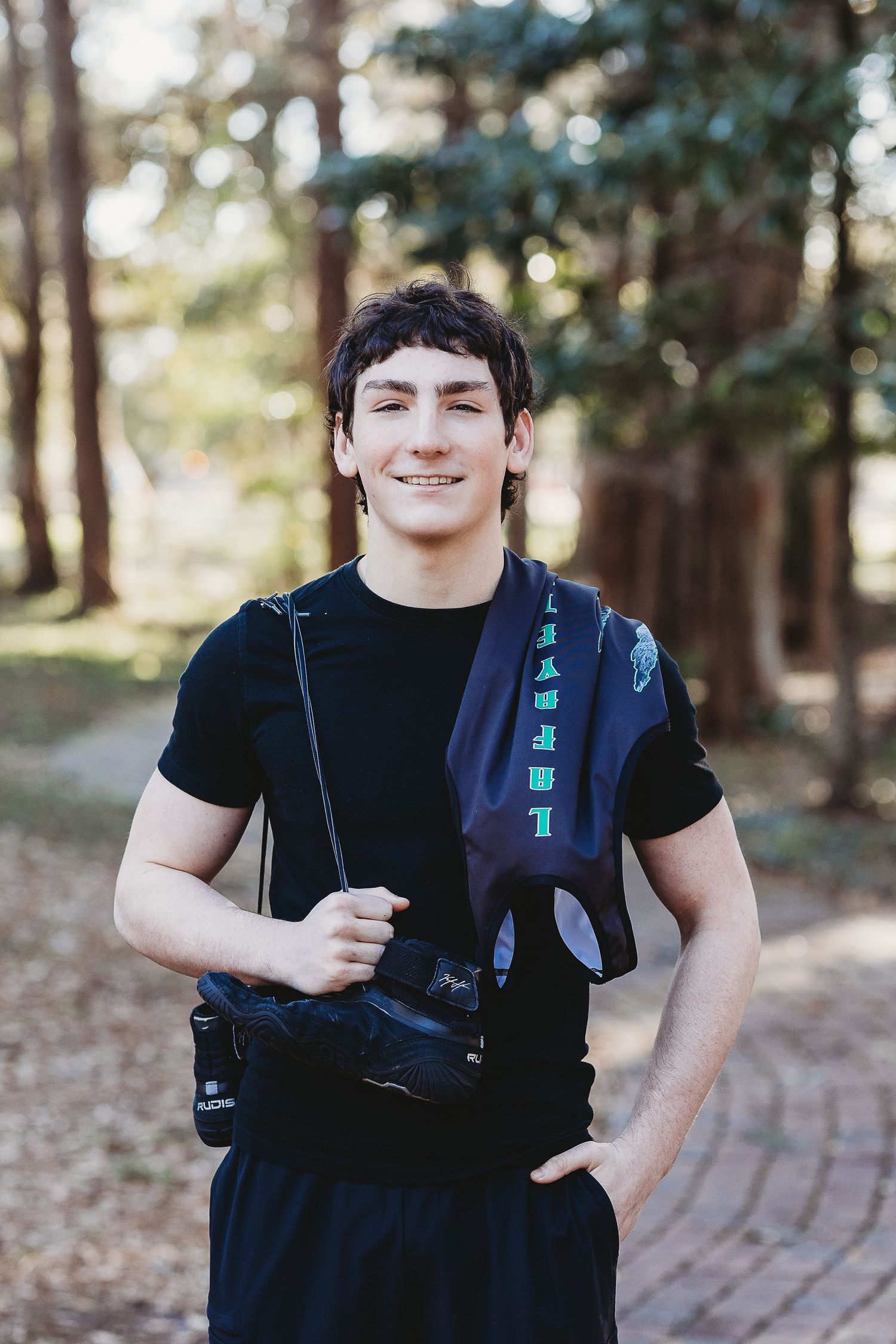 Student photographer with camera gear standing on brick path in wooded area.