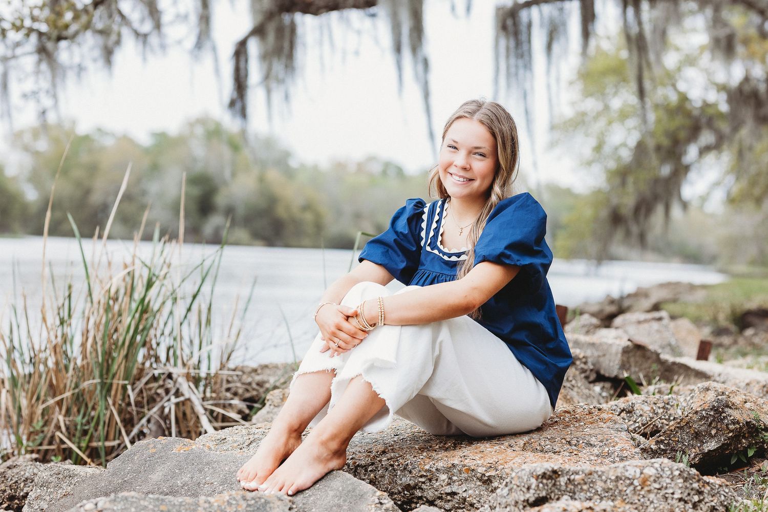 Outdoor portraits by the water featuring someone in a navy dress relaxing on natural terrain.
