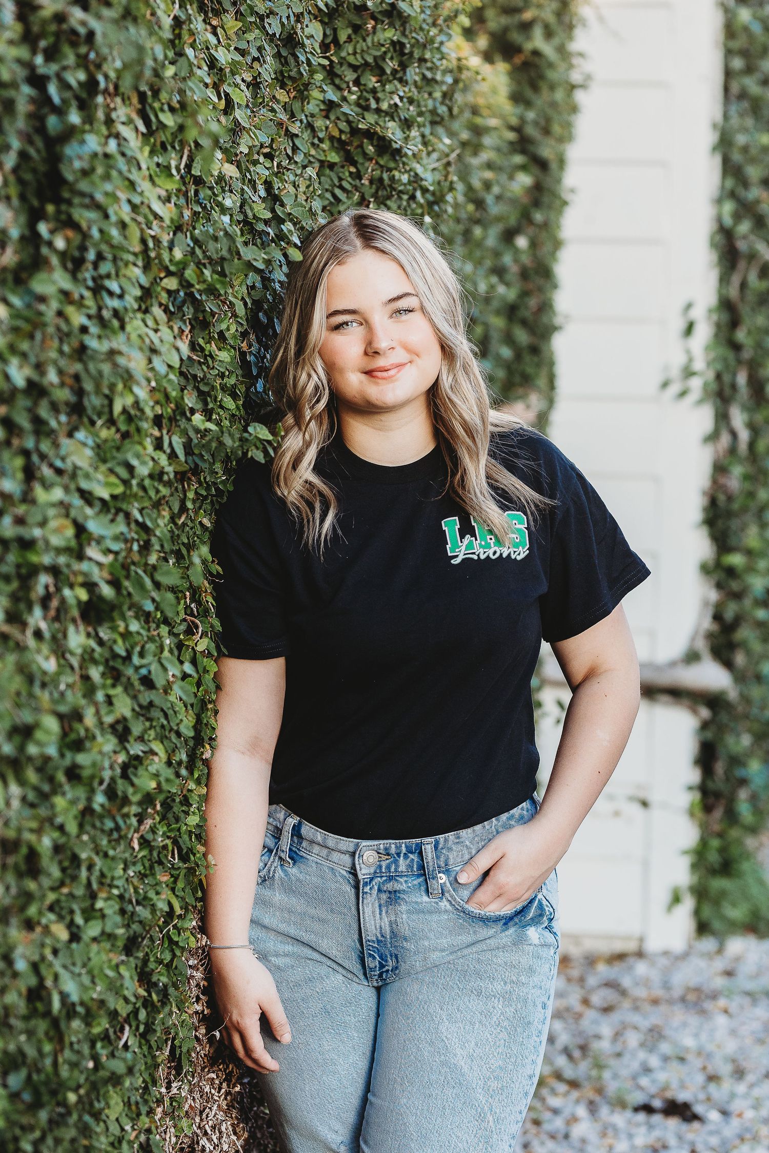 Lifestyle portrait against ivy wall wearing black logo tee and classic denim.