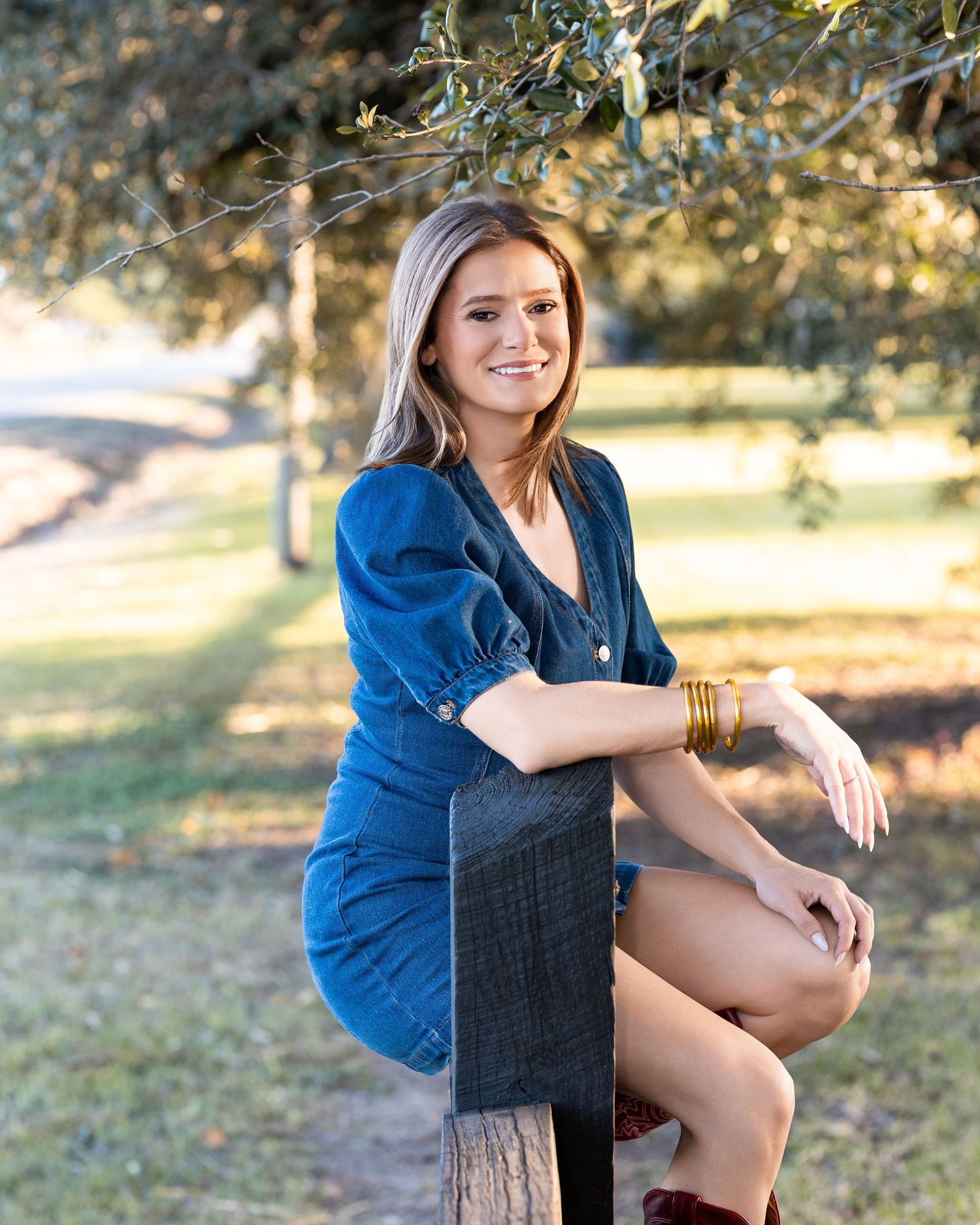 A woman in a denim jacket sits on a dark chair outdoors in natural lighting with a warm autumn setting.