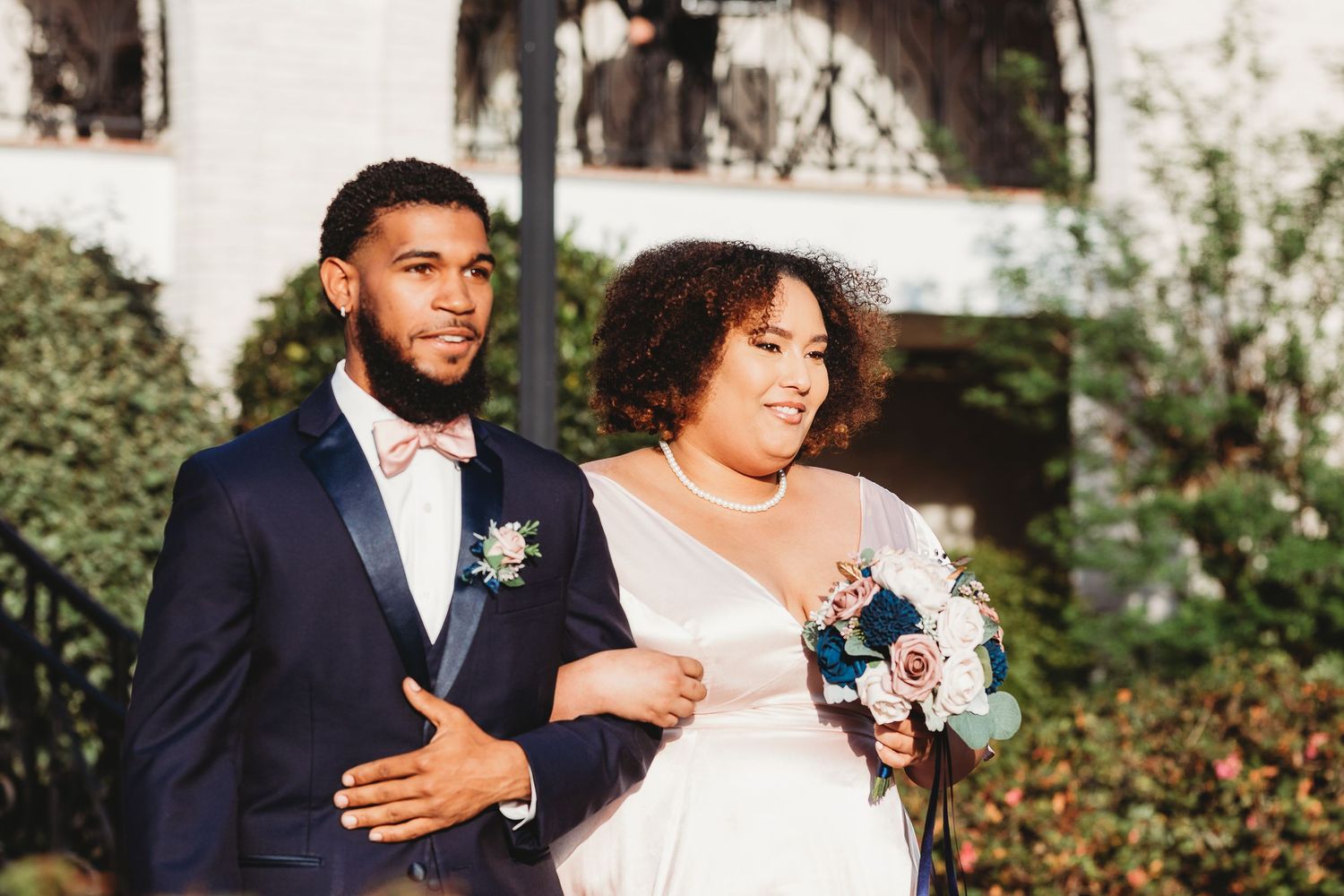 Wedding party members share candid laughs and embraces in outdoor garden setting.