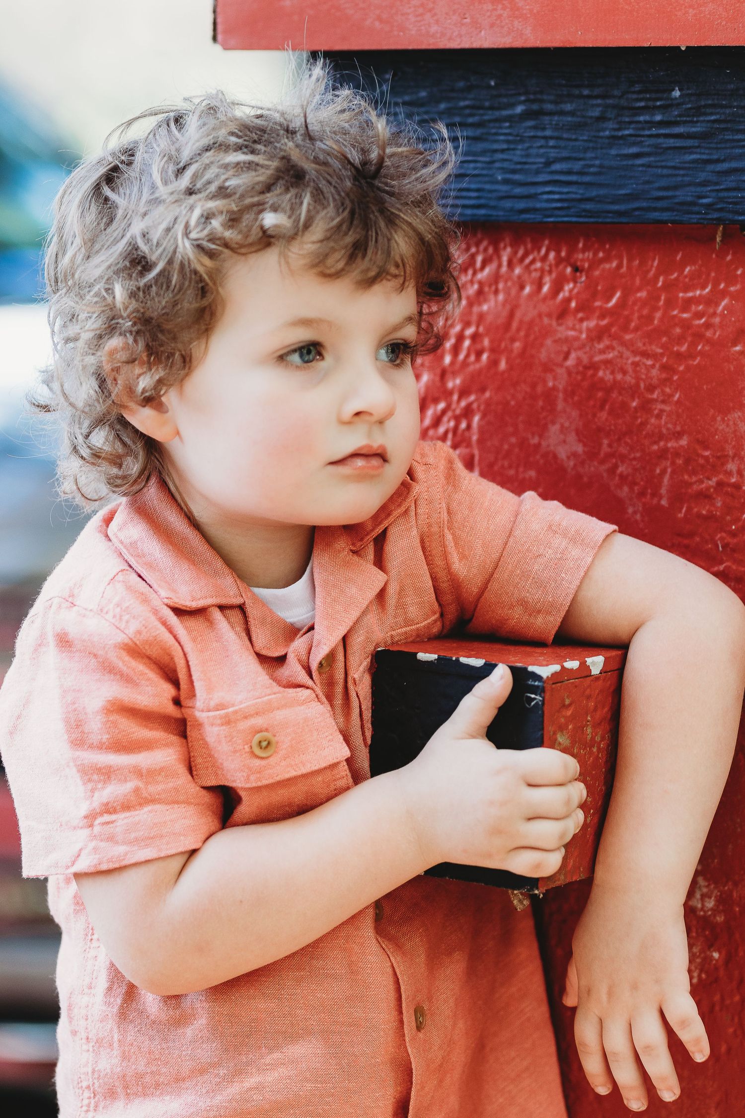 Child in coral shirt sitting against bright red background in candid poses.