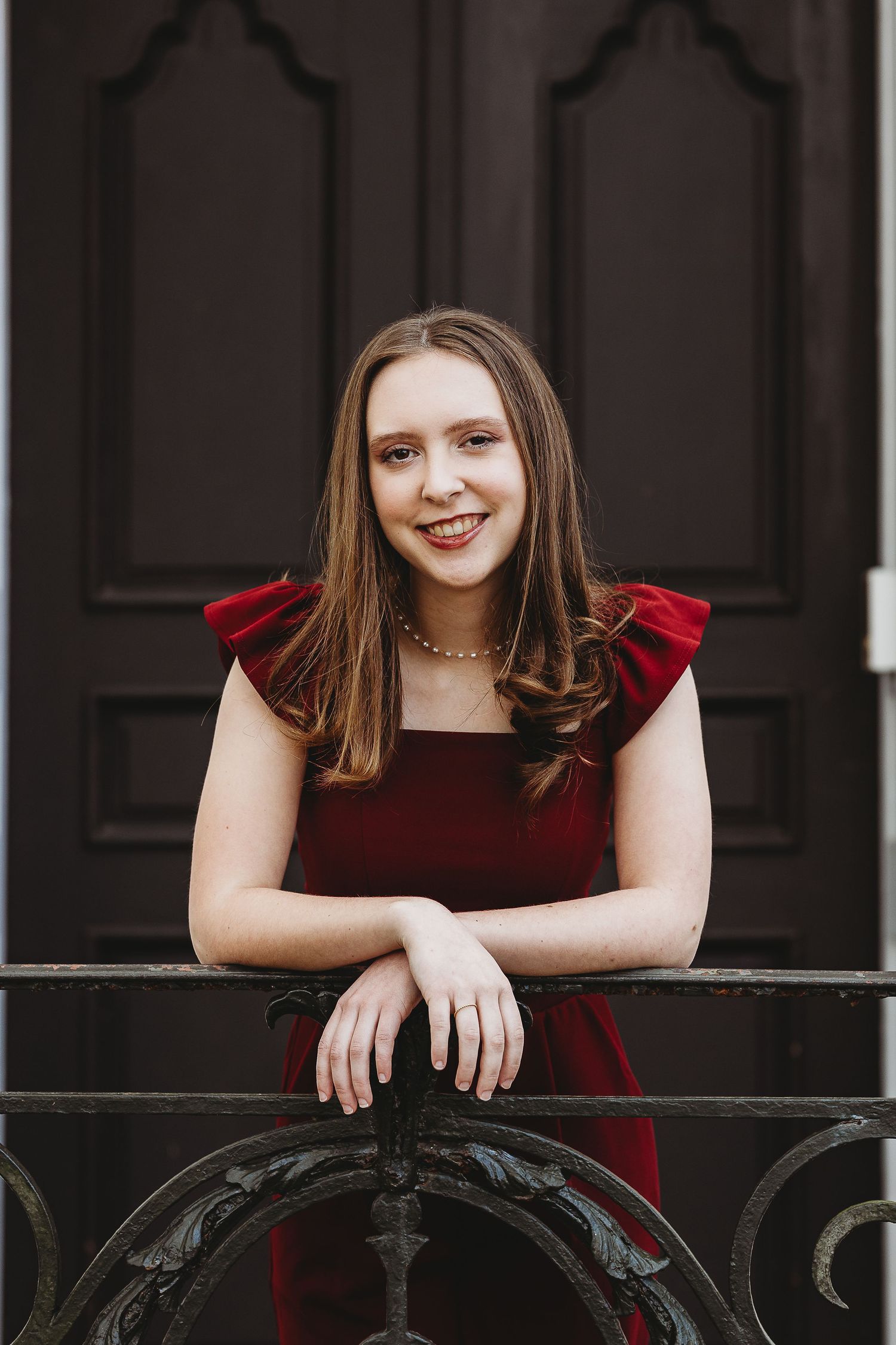 A dancer in a red velvet dress poses elegantly against an ornate black door.