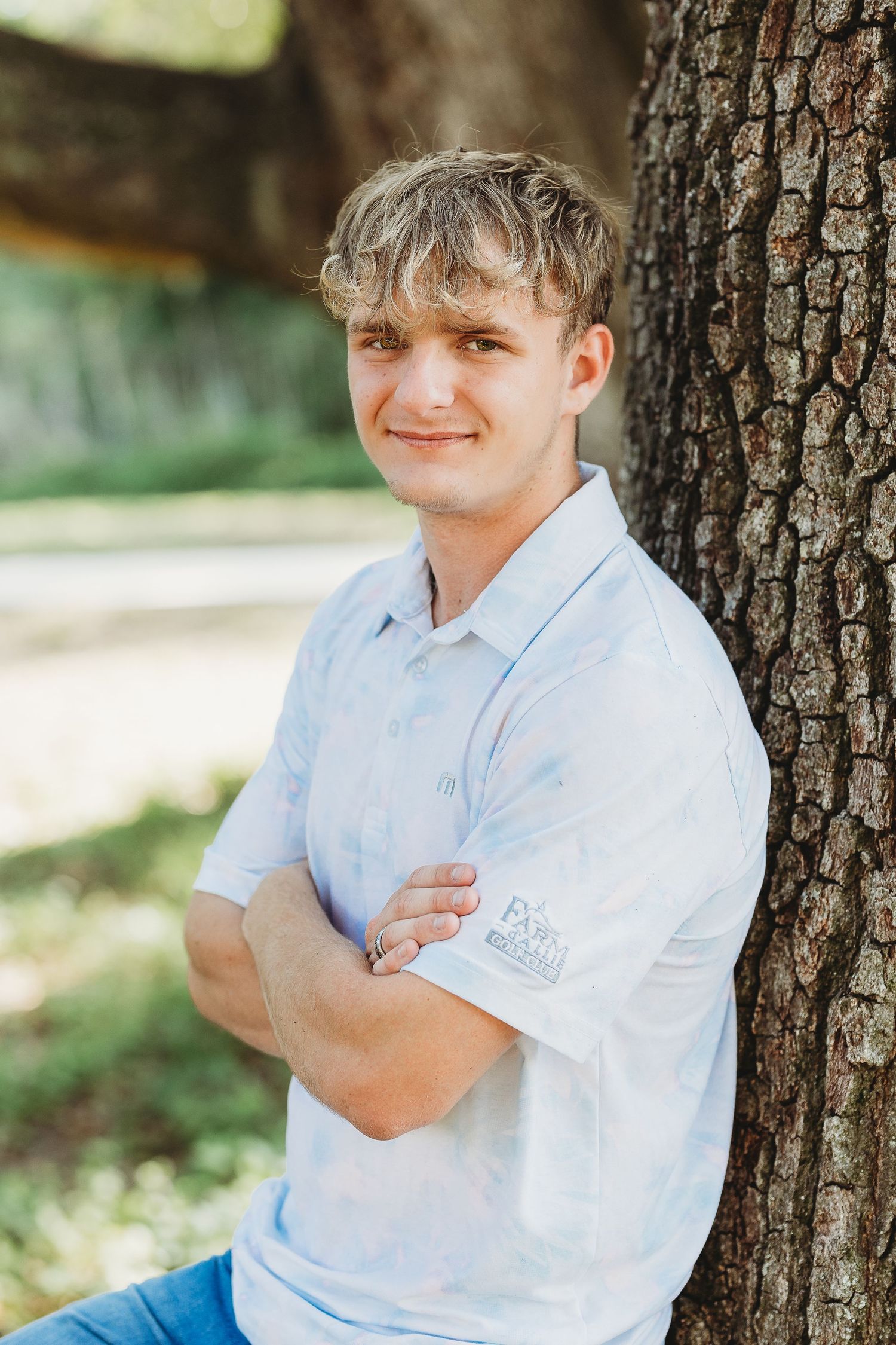 Casual outdoor portrait leaning against tree trunk in white polo shirt.