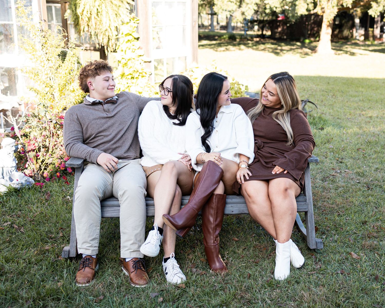 A group sits casually on grass during an outdoor photo session in warm sunlight.