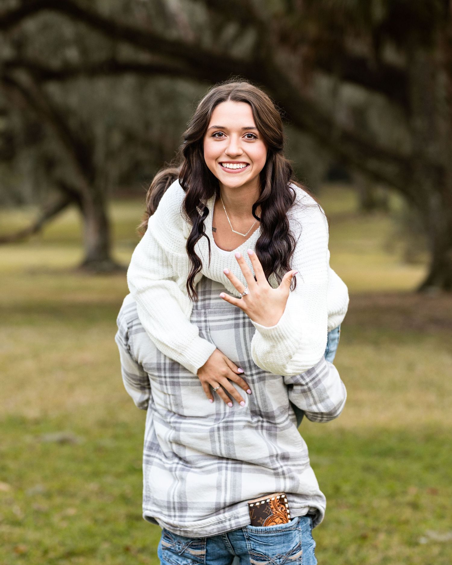 A person in a plaid shirt and jeans stands in a grassy outdoor setting making expressive poses and gestures.