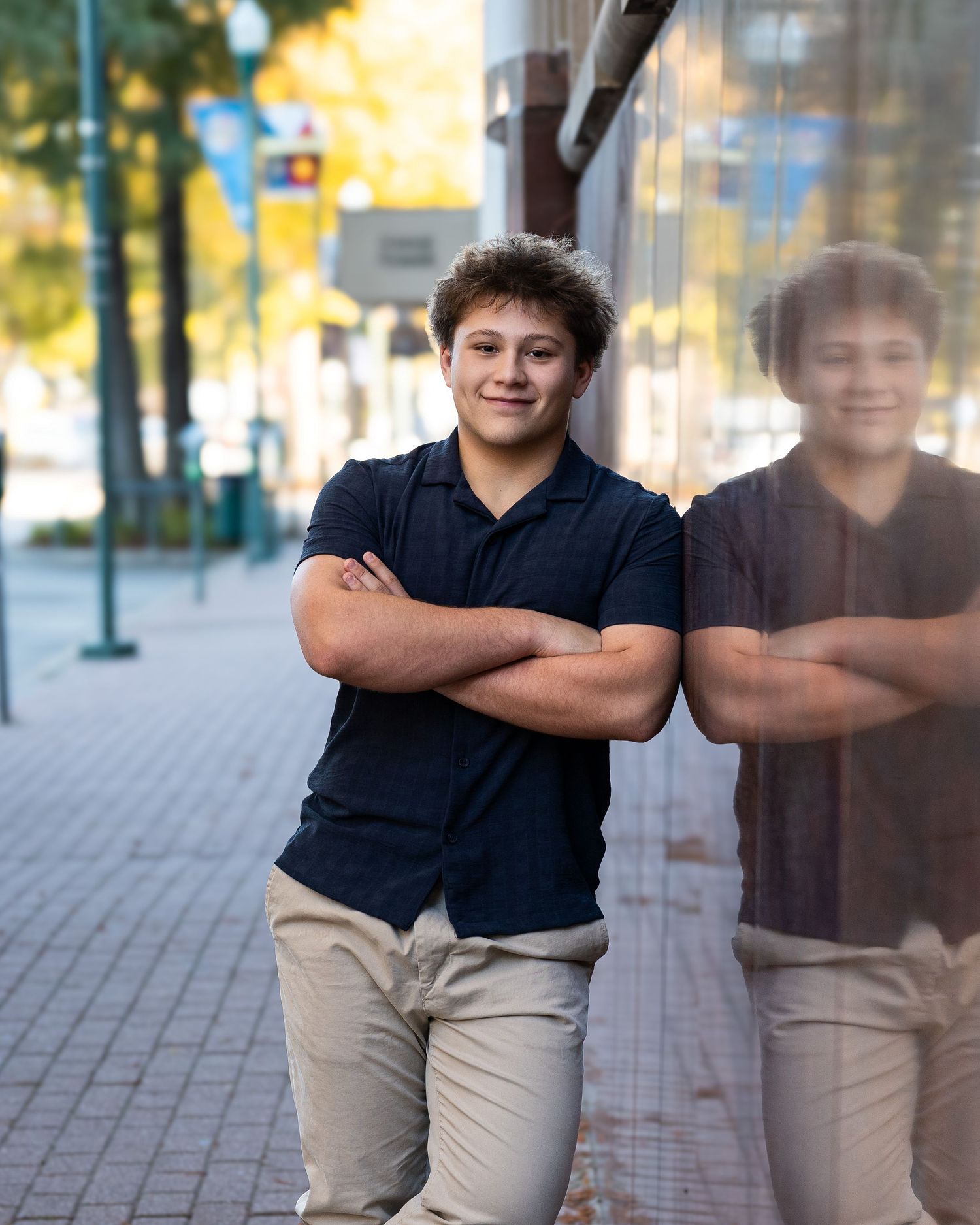 A person in a black shirt and khaki pants leans against a reflective surface outdoors creating a mirror effect.