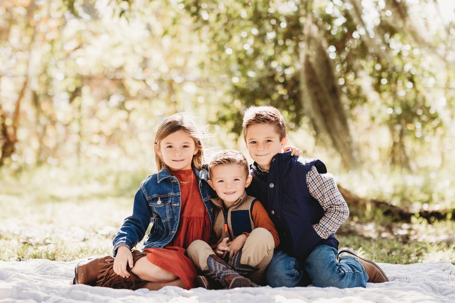 Casual family photo session with siblings lying on grass in outdoor setting.