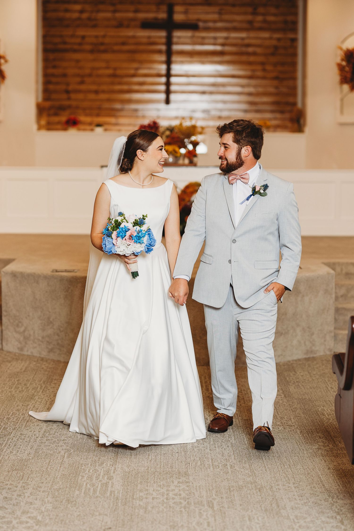 Wedding couple walking together in a church hallway with brick walls and wooden pews.