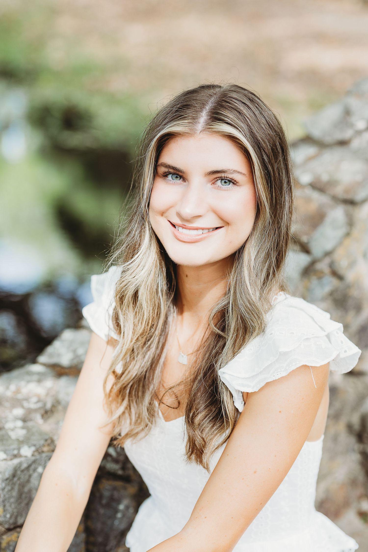 Person in white ruffled top smiling while posing against natural stone background.