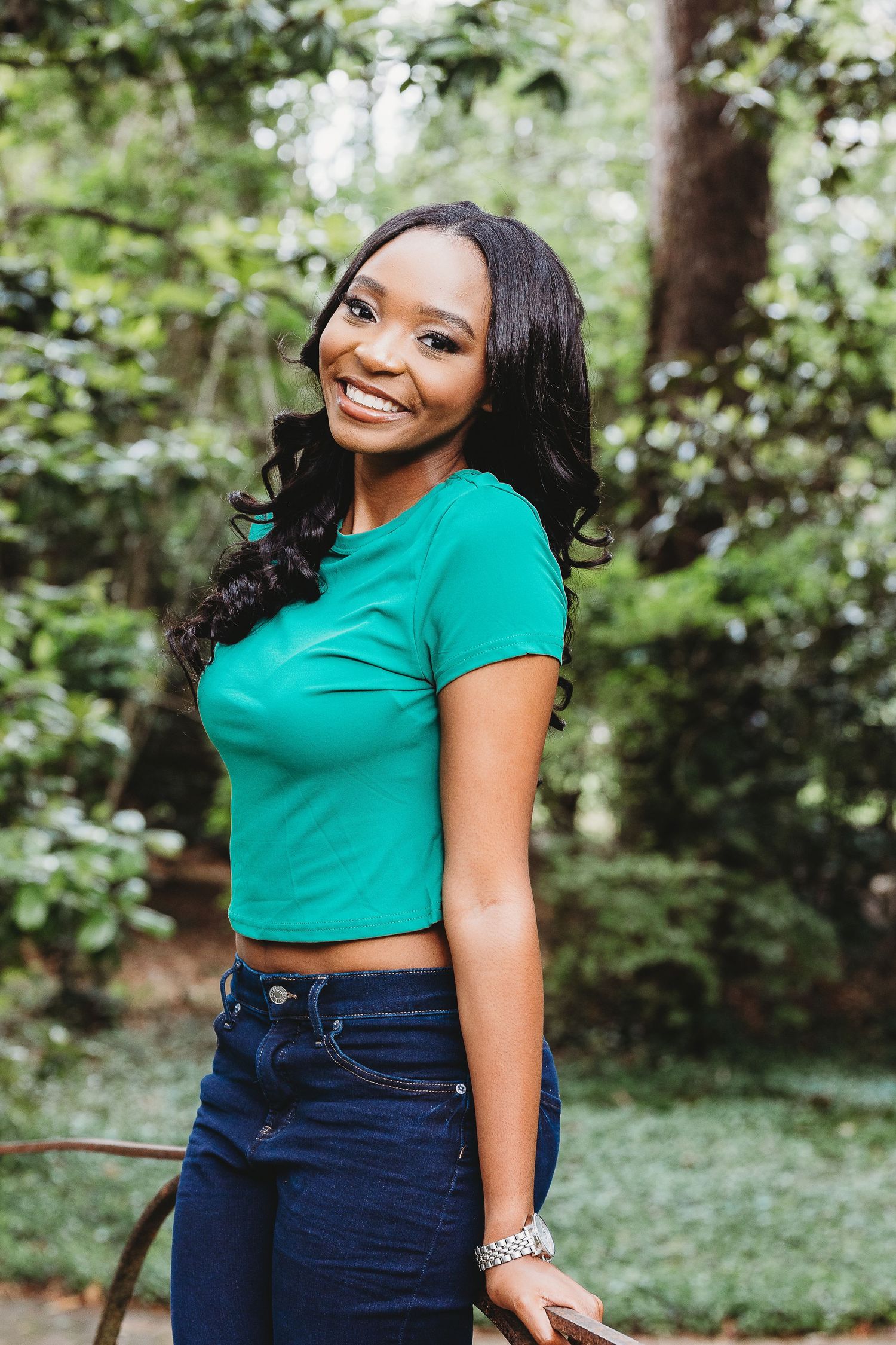 Stylish summer outfit featuring a cropped teal top and navy jeans in a garden setting.