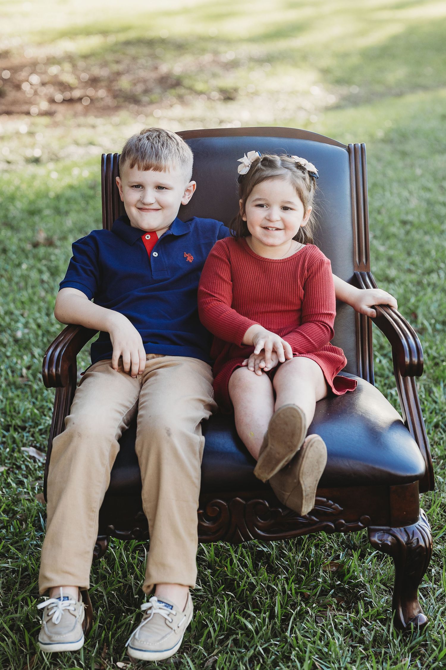 Siblings sitting together on dark leather bench outdoors.