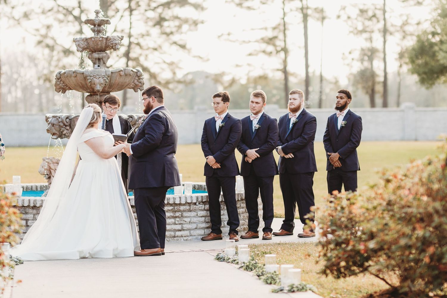 Outdoor wedding ceremony setup with stone fountain and pine trees creating a romantic backdrop.