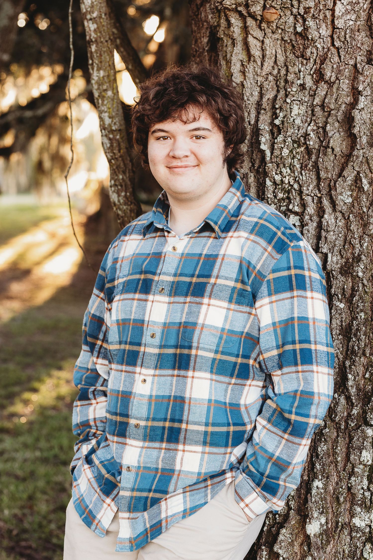 Portrait series against a tree trunk wearing a blue plaid shirt.