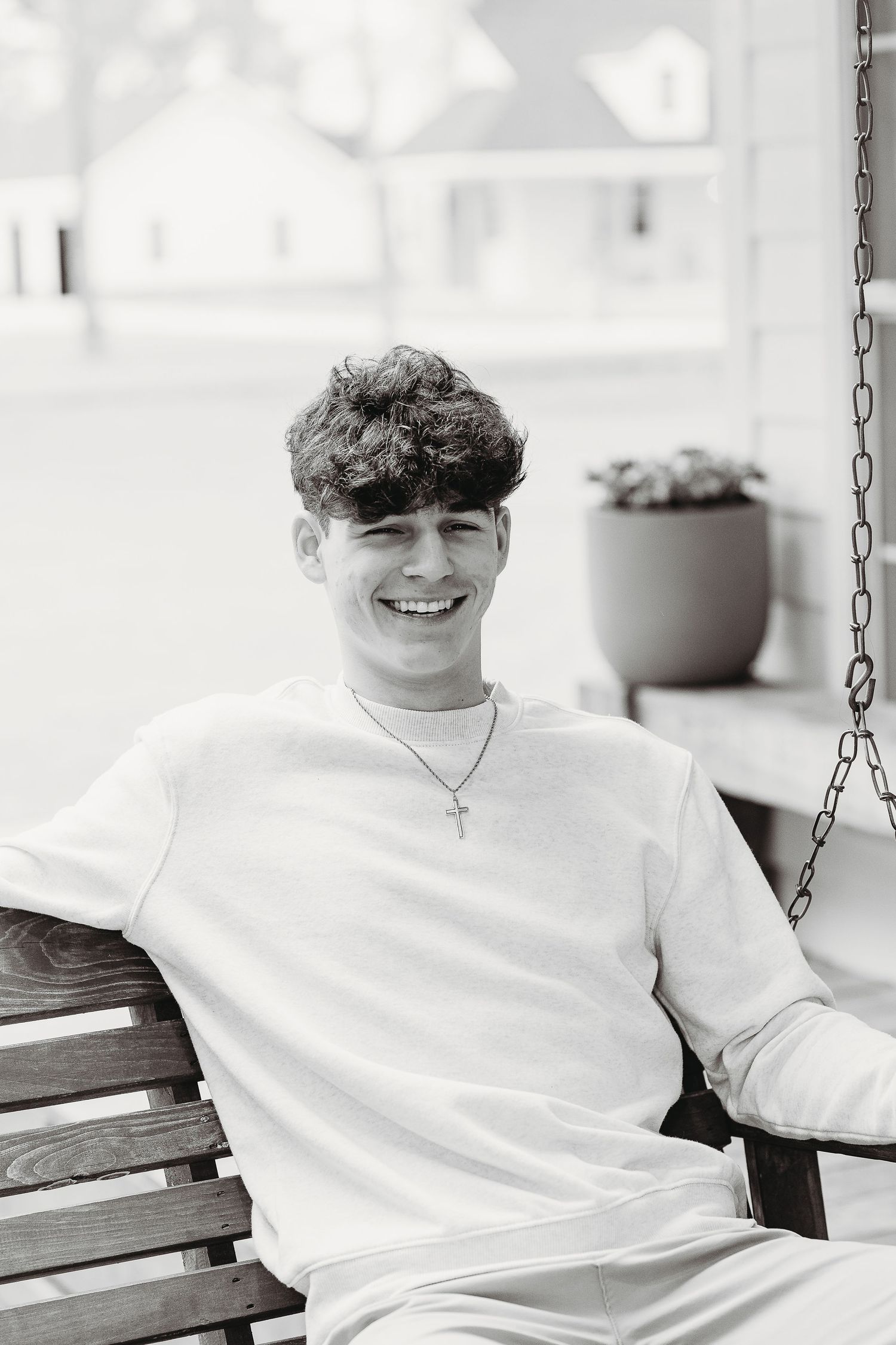 Black and white portrait of person relaxing on wooden porch swing.