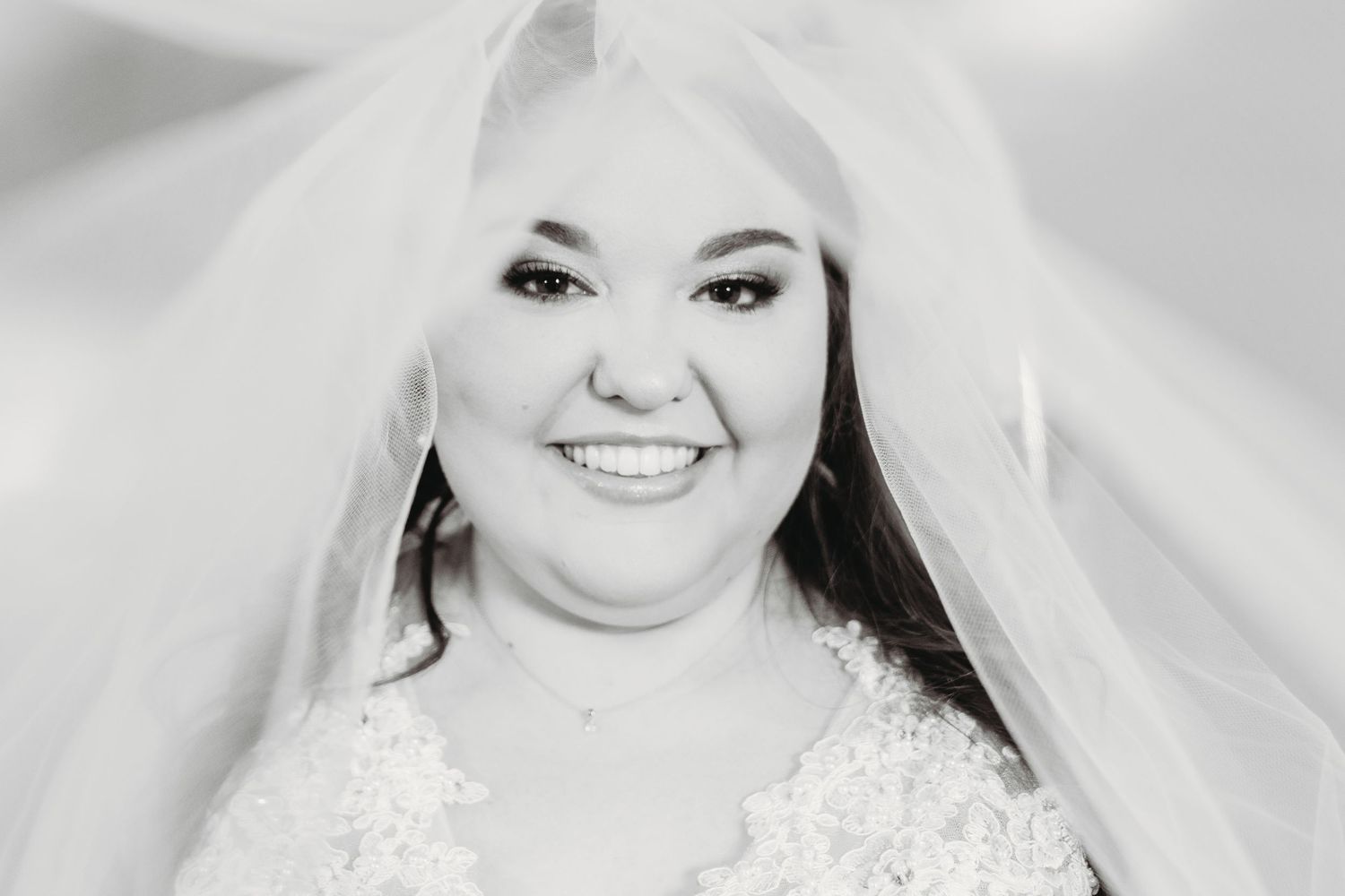 Bride wearing a white wedding dress smiles radiantly in a classic bridal portrait.