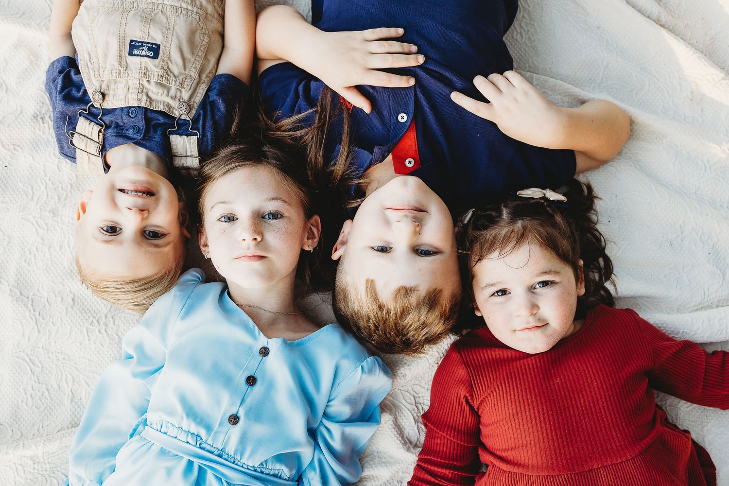 Children in coordinated outfits lying together on white backdrop.