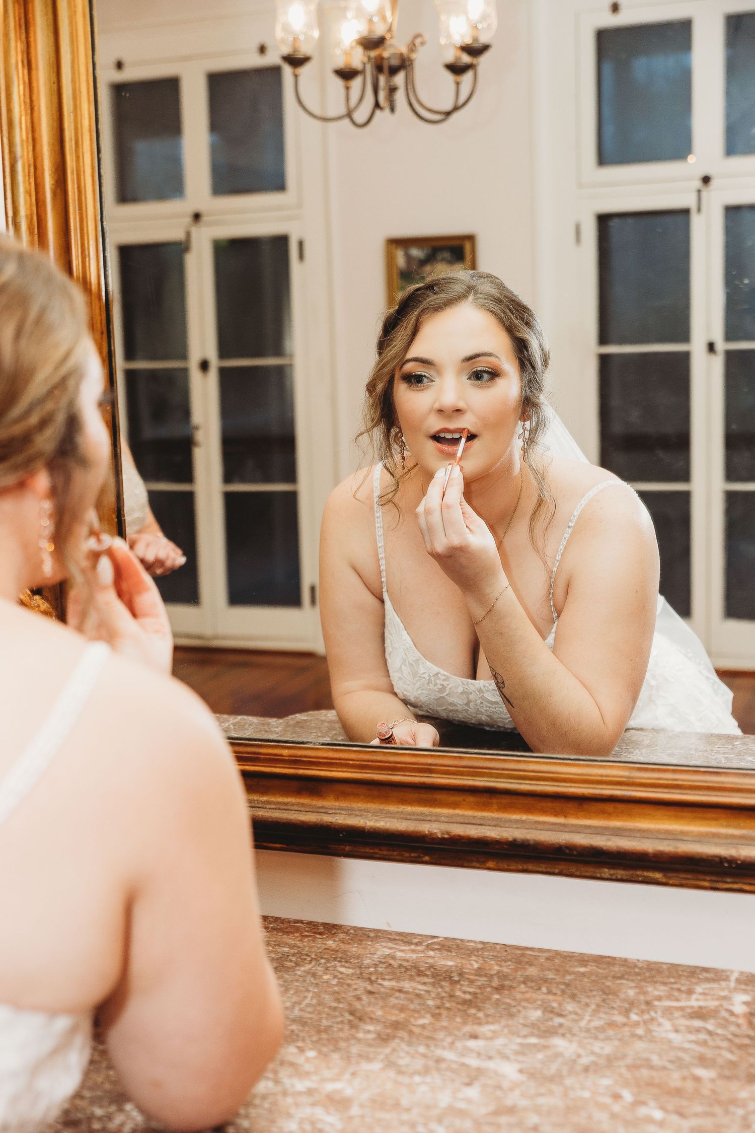 Bride applies lipstick while looking in an elegant mirror during wedding preparations.
