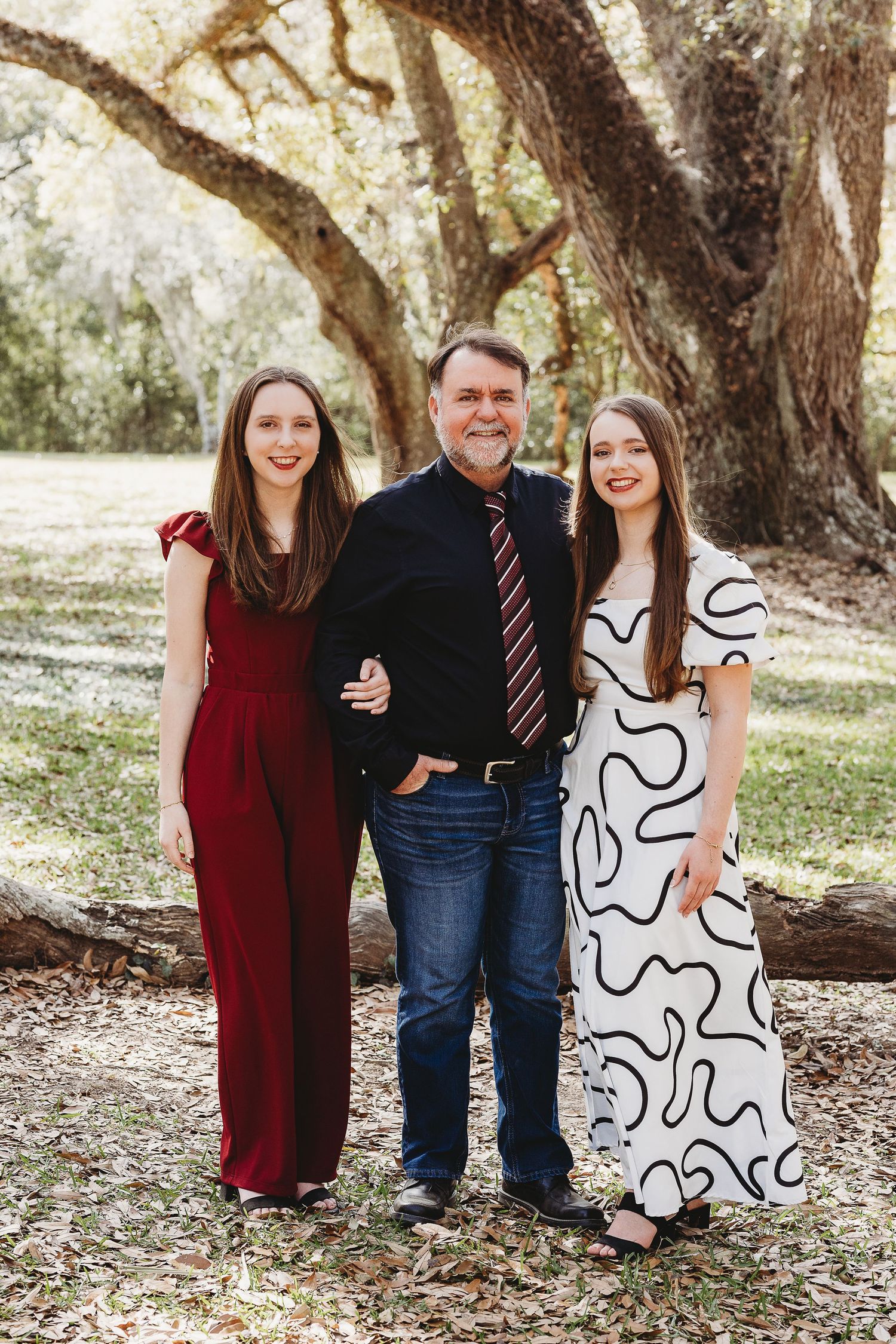 A family group photo under oak trees with members wearing coordinated burgundy, black and white outfits.