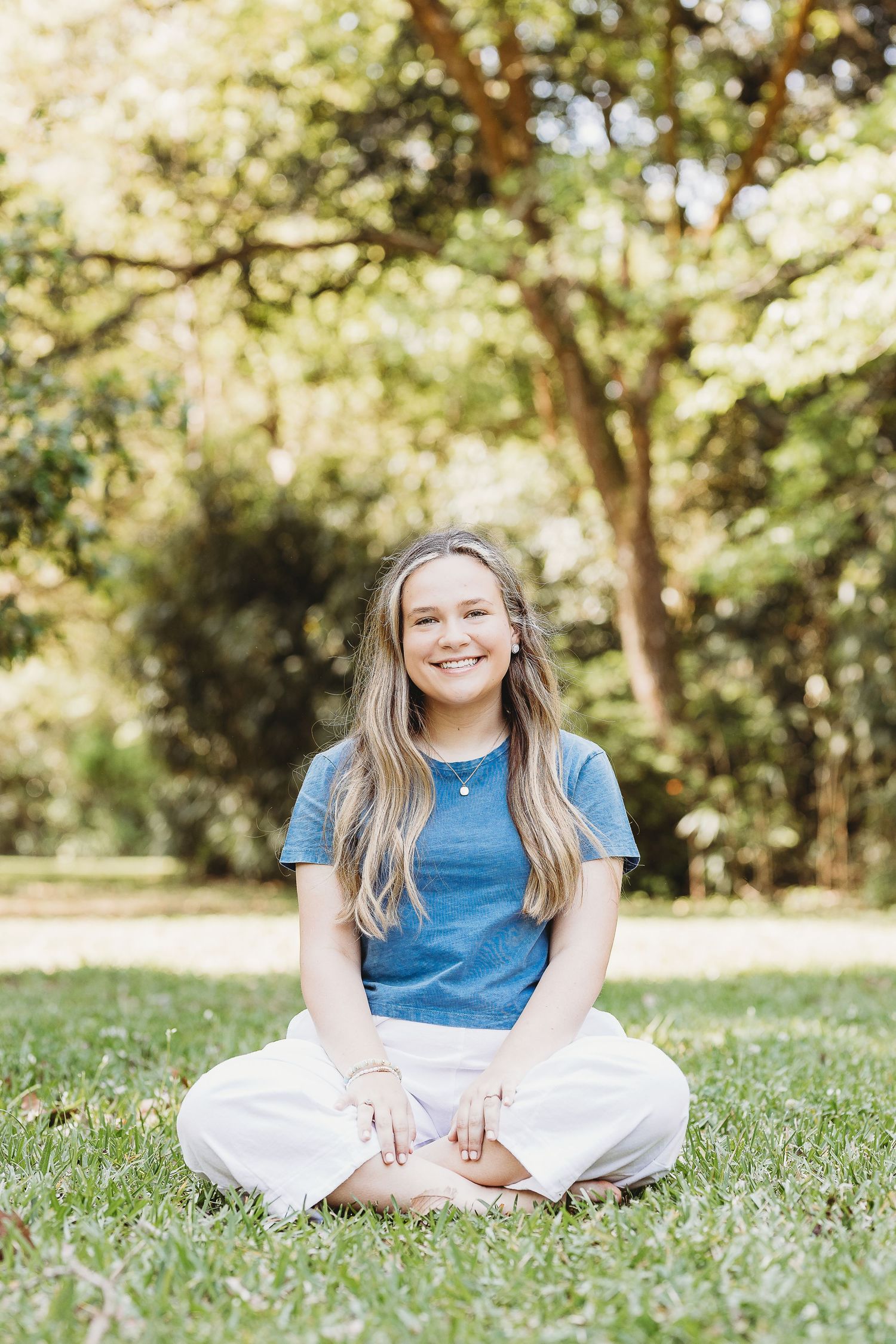 Casual outdoor portrait sitting on grass in blue shirt and white pants on sunny day.
