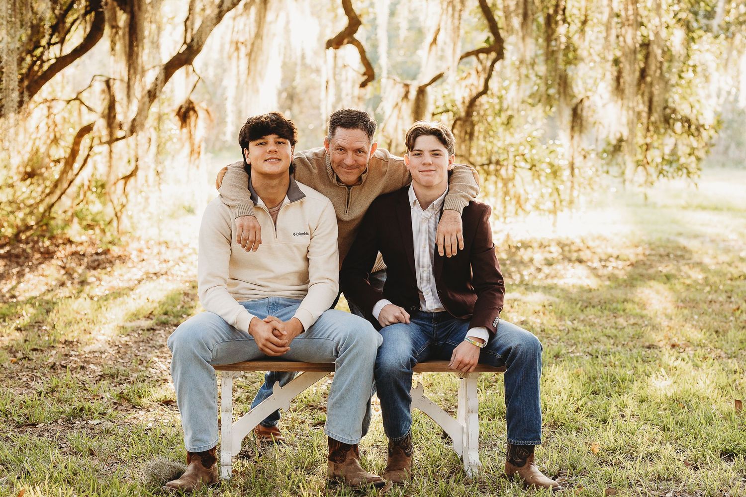 Family group sitting casually together on grass with Spanish moss trees in background.