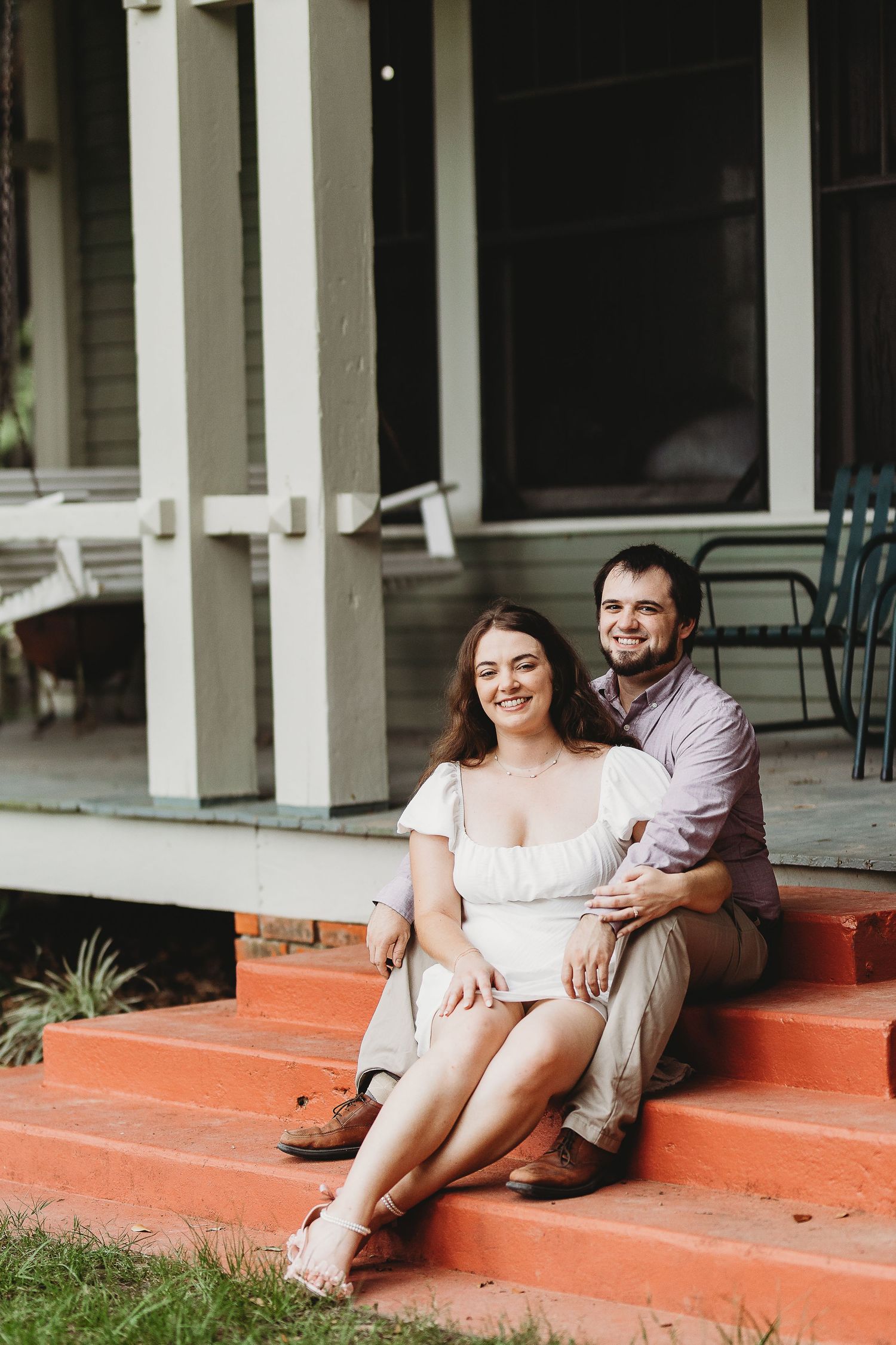 A couple sits together on red brick steps outside a building with white columns.