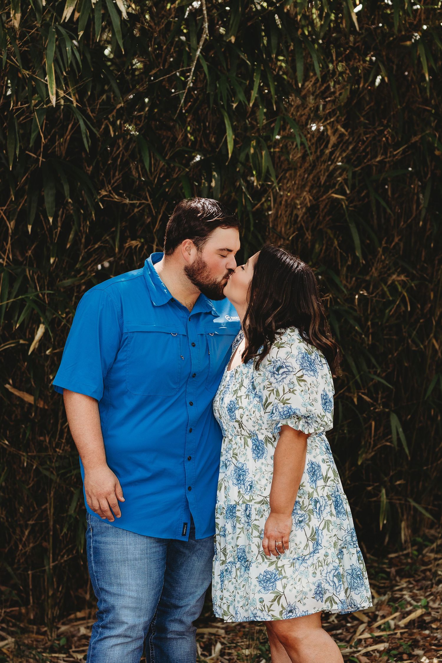 Couple in blue and floral outfits posing together against bamboo backdrop.