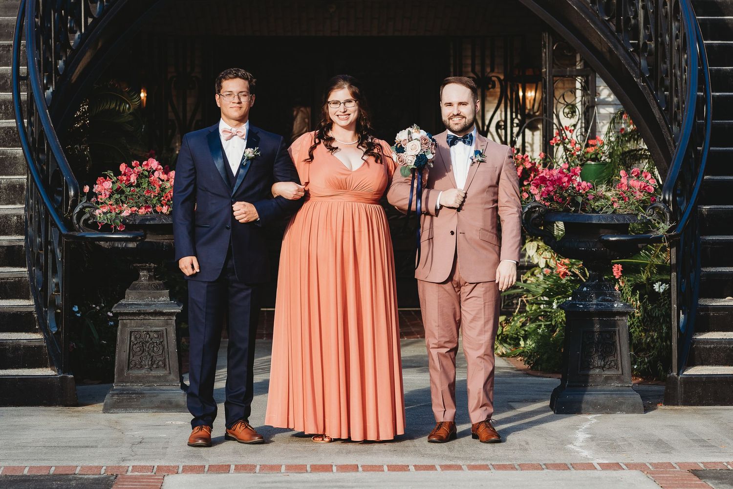 Wedding party lined up on steps wearing mix of coral and neutral formal attire.
