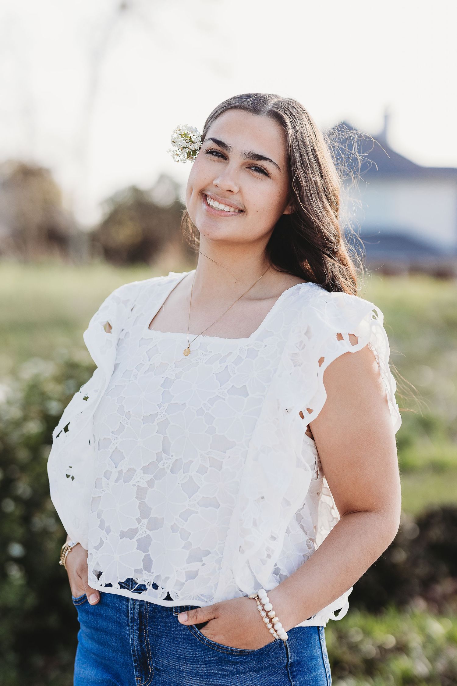 Casual portrait wearing white eyelet top and jeans against natural outdoor background.