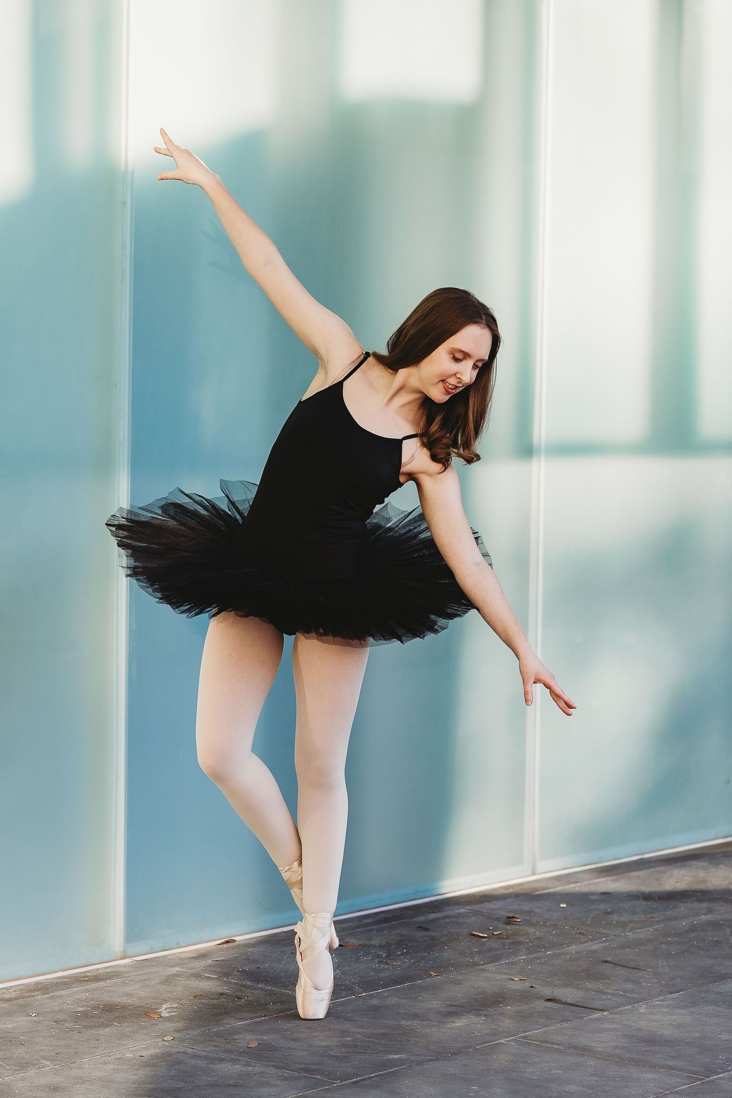 A ballerina in a black tutu performs an arabesque pose in front of a modern backdrop.
