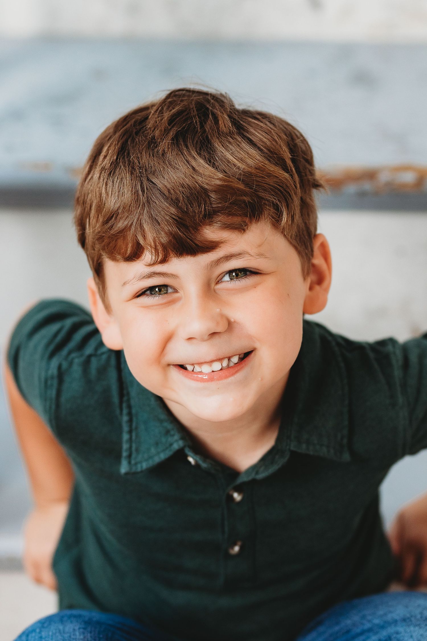 Close up portrait of a child in a green polo shirt smiling brightly.