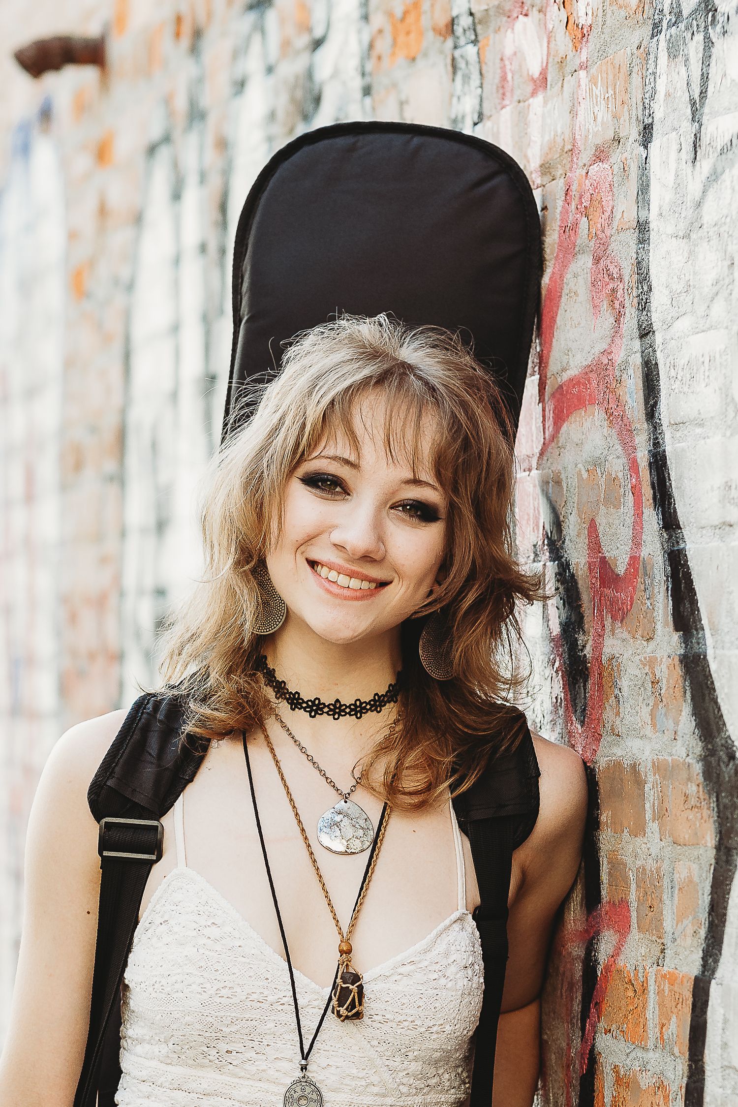 Woman in white lace dress poses against graffiti wall with vintage style accessories.