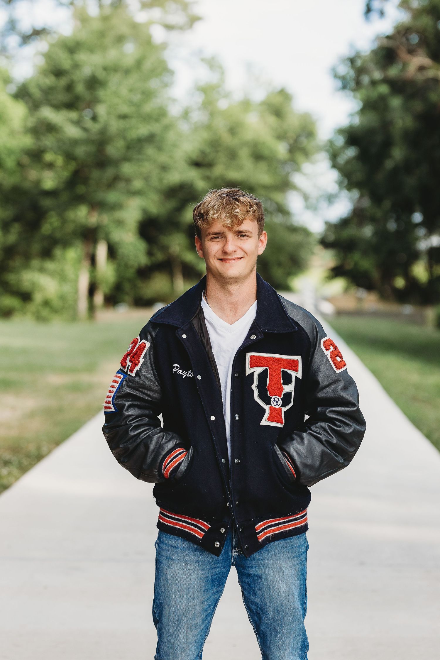 Casual outdoor portrait of student in black varsity jacket with red and white lettering.