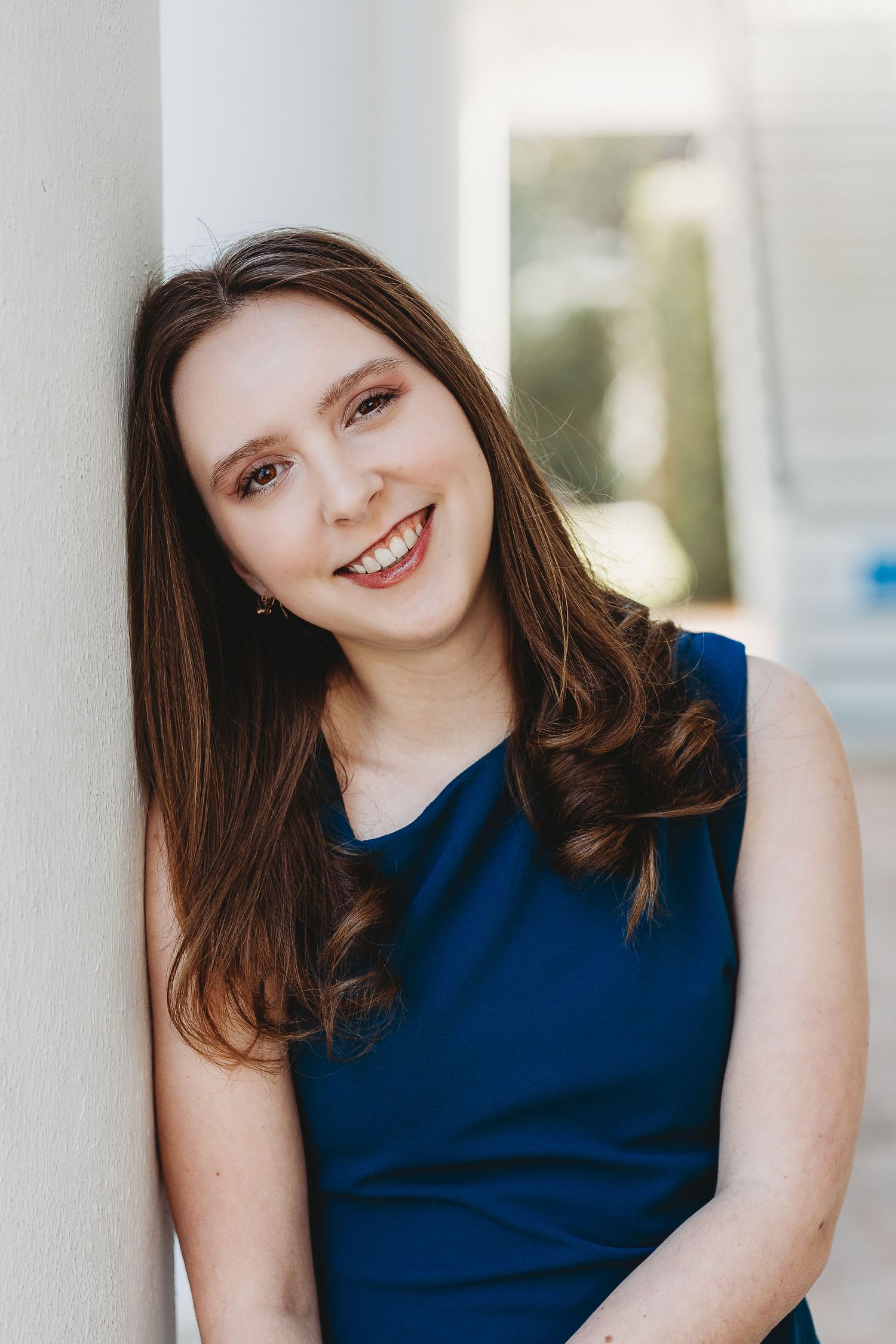 Portrait against white column wearing navy blue sleeveless dress.