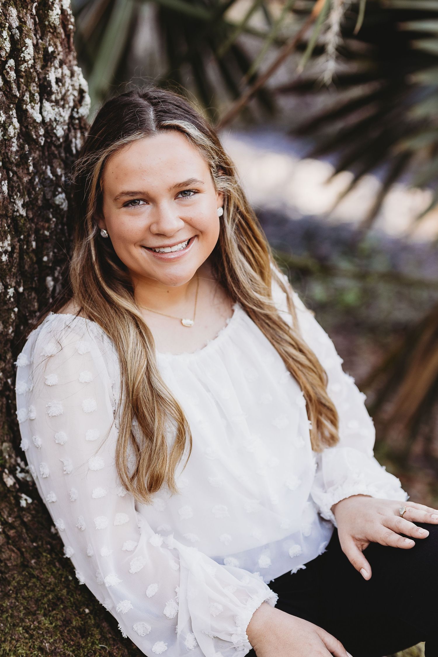 Person wearing white textured blouse poses against tree trunk during outdoor photo shoot.